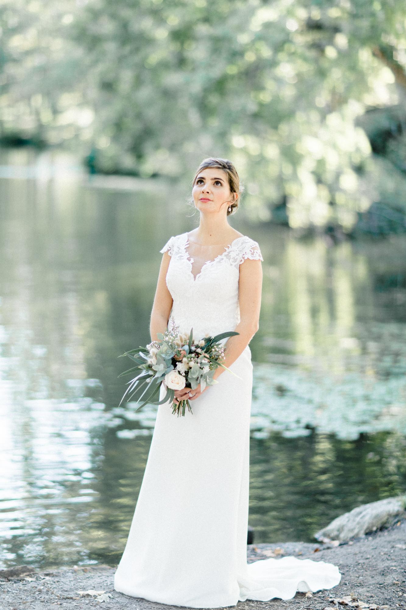 Bride standing by the pond in Parc de Majolan, bouquet in hand