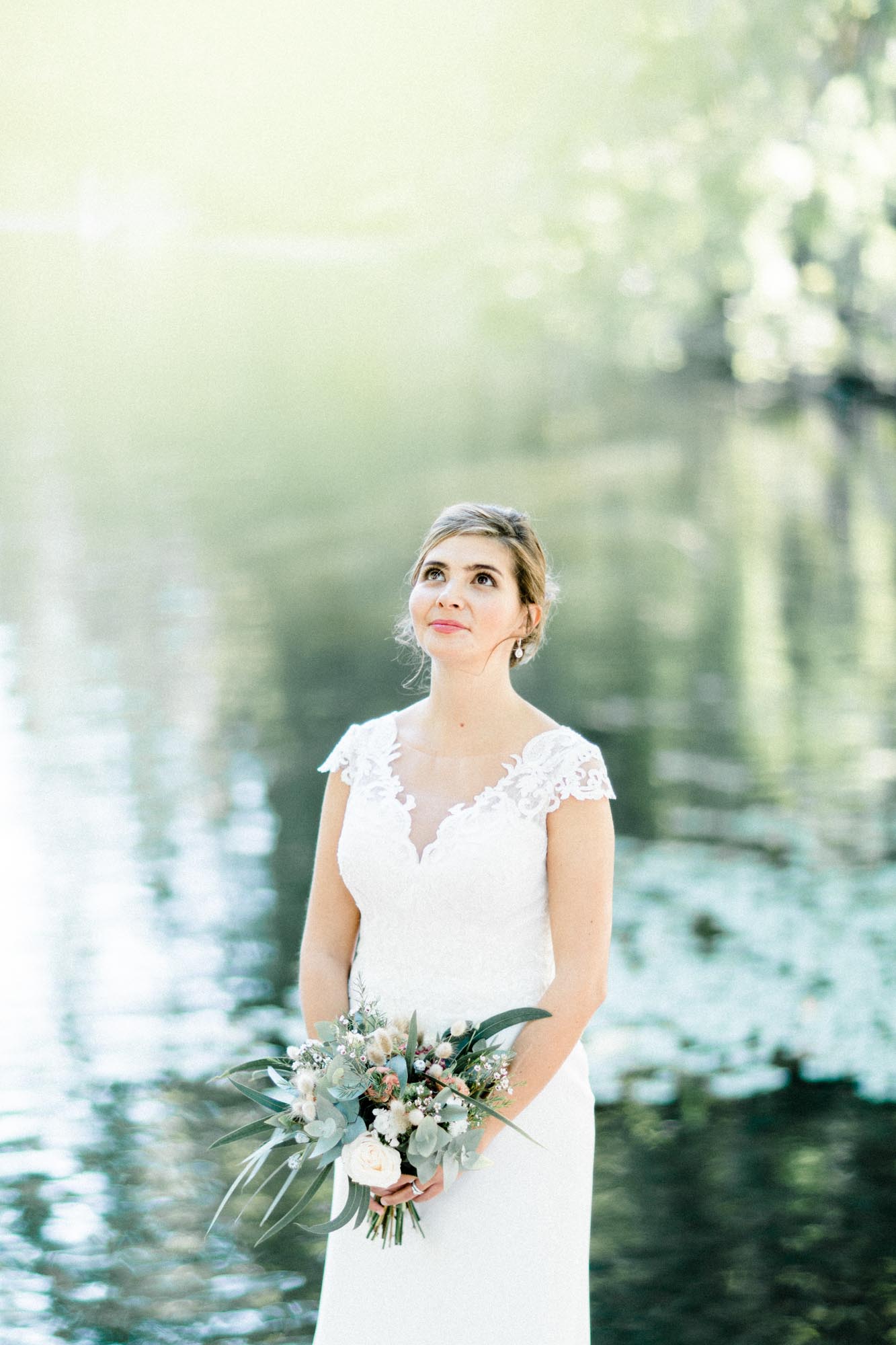 Bride gazing into the distance by the sparkling pond