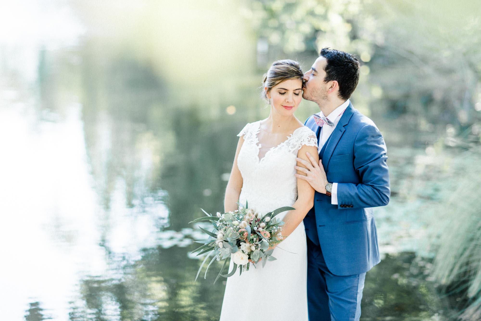 The groom kissing the bride's temple by the pond