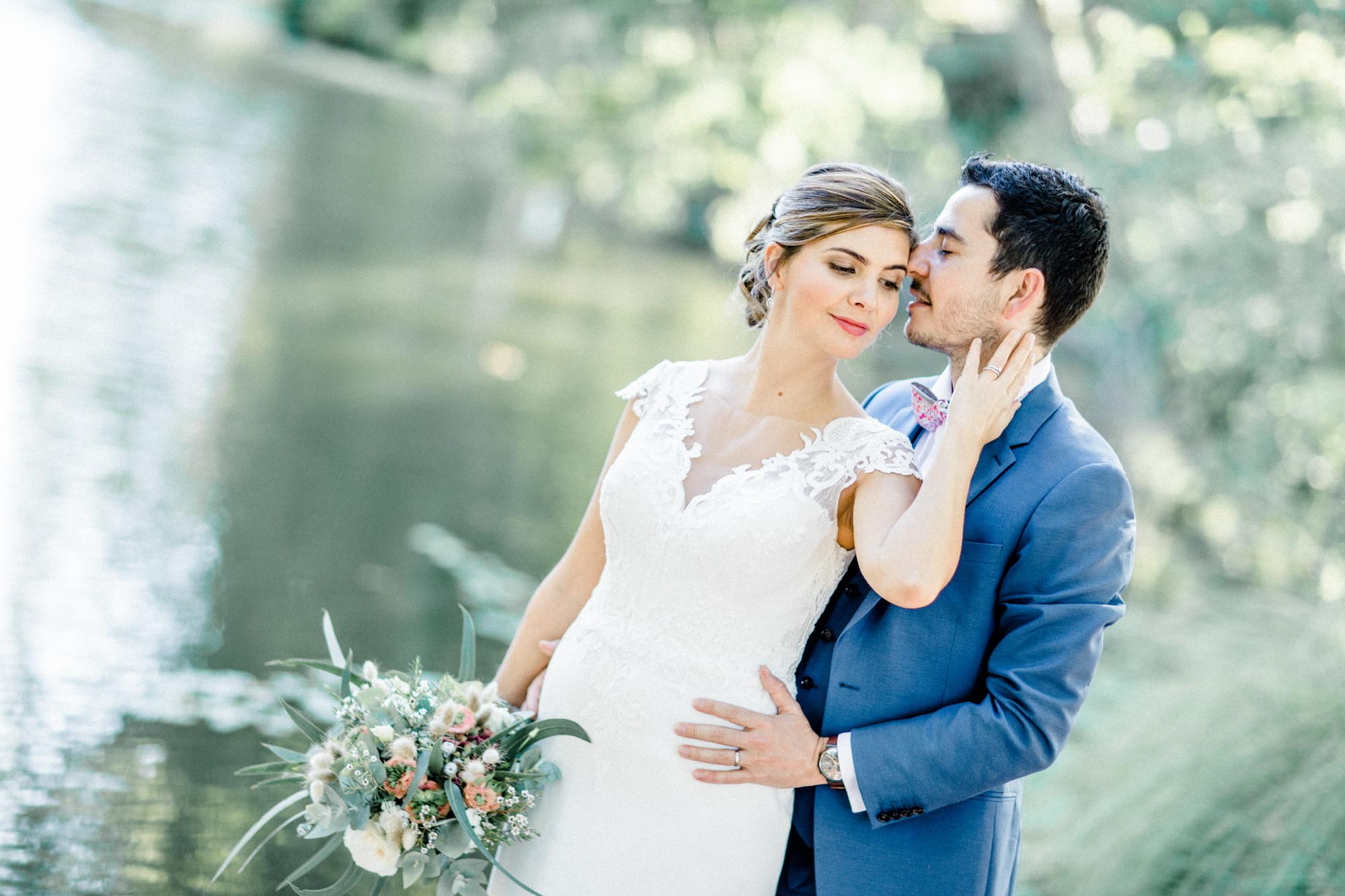 Bride with her hand on the groom's cheek by the park pond