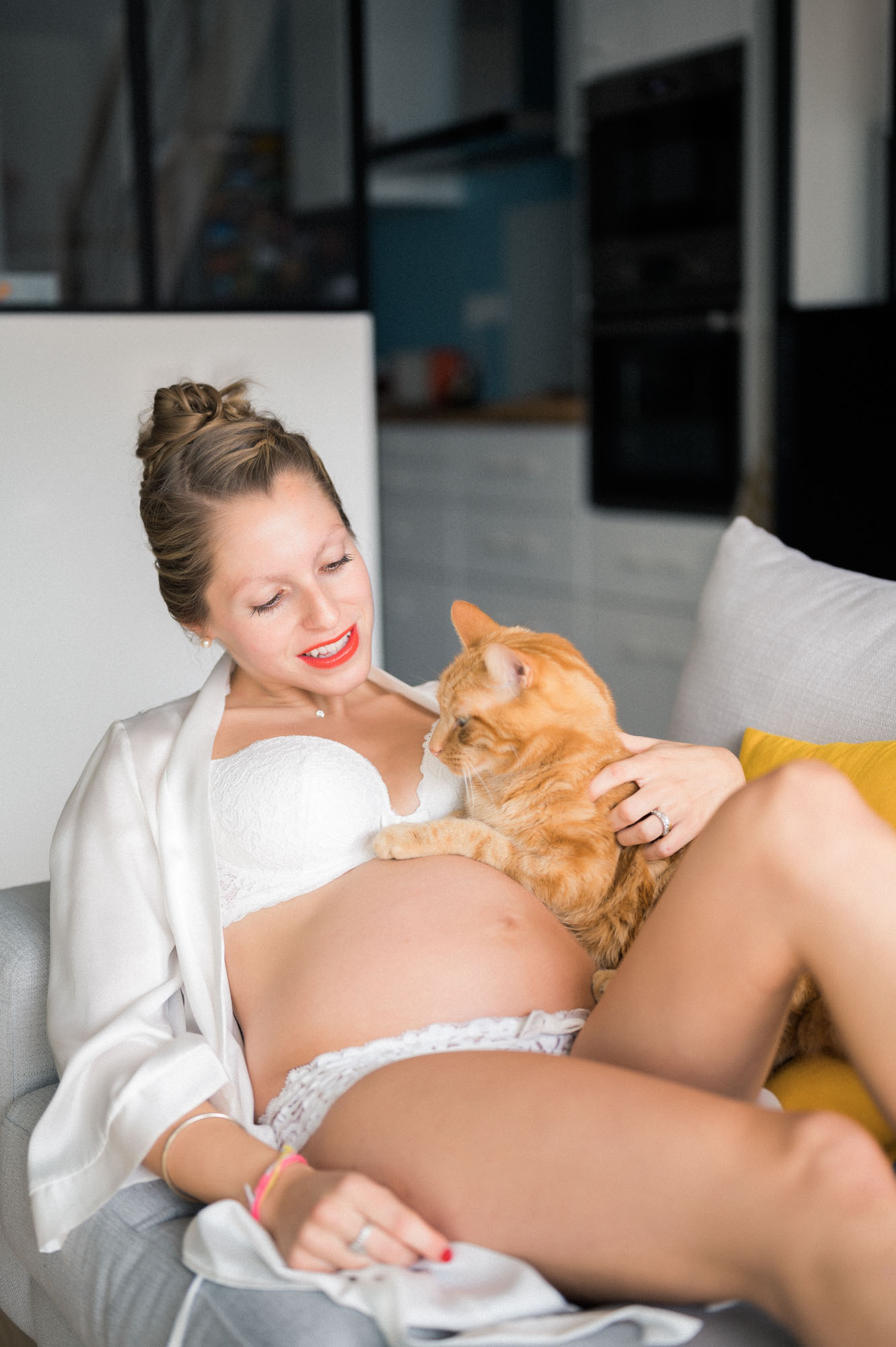 Mum-to-be in white lingerie cuddling her ginger cat on the sofa