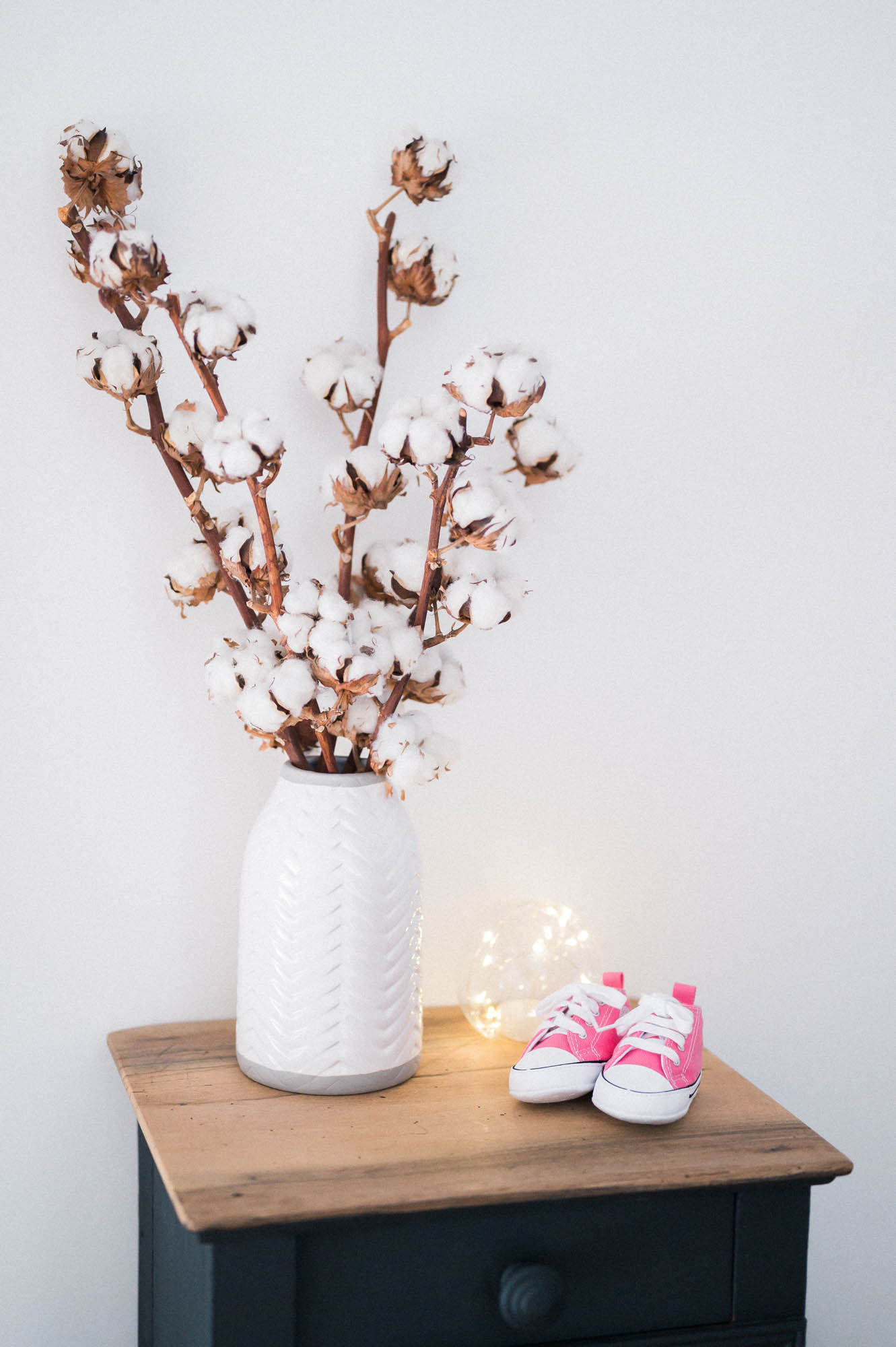 Vase of cotton branches and tiny pink trainers on a chest of drawers