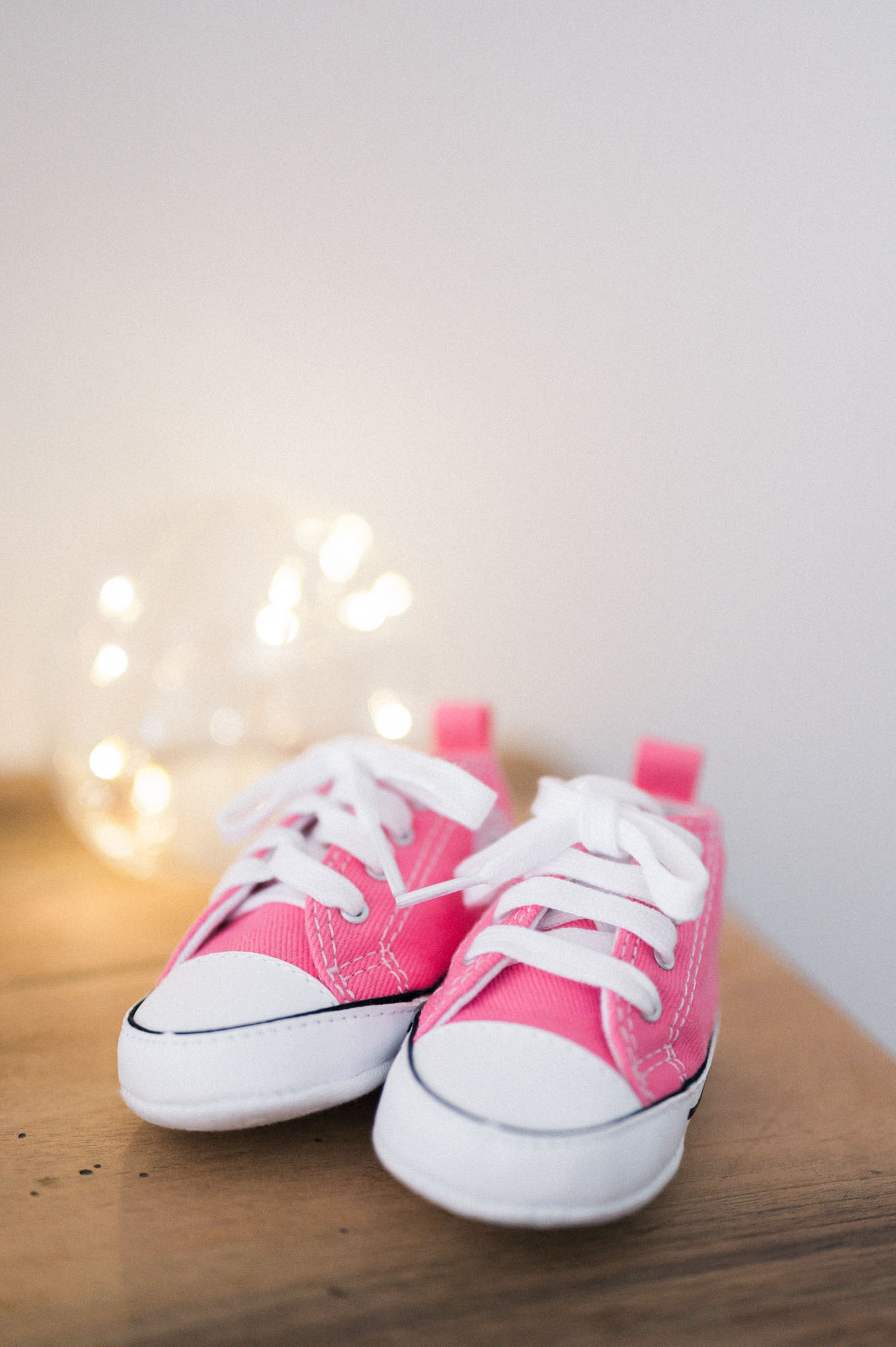 Tiny pink baby trainers in front of fairy lights