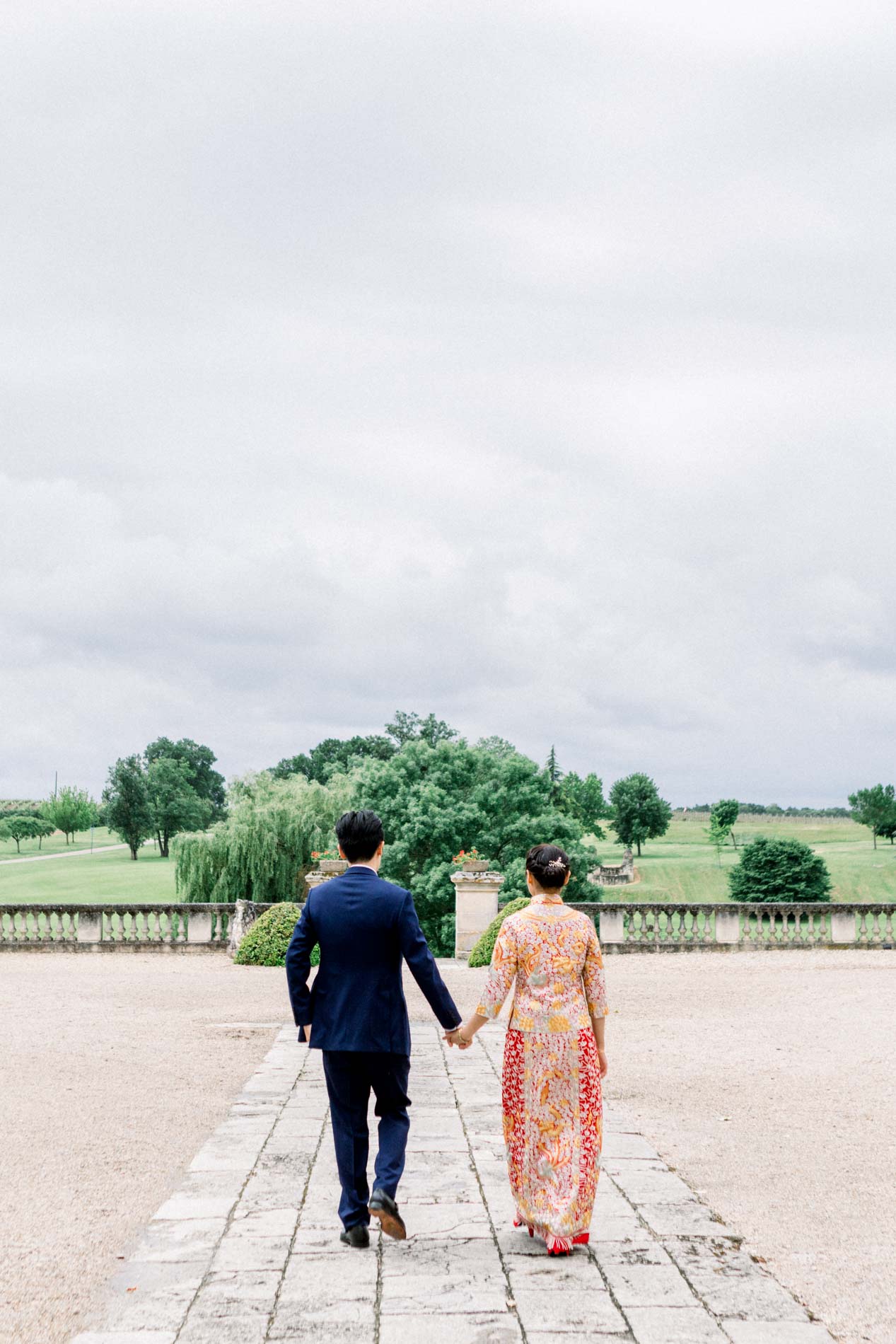 The couple walking hand in hand along the path at Château des Vigiers
