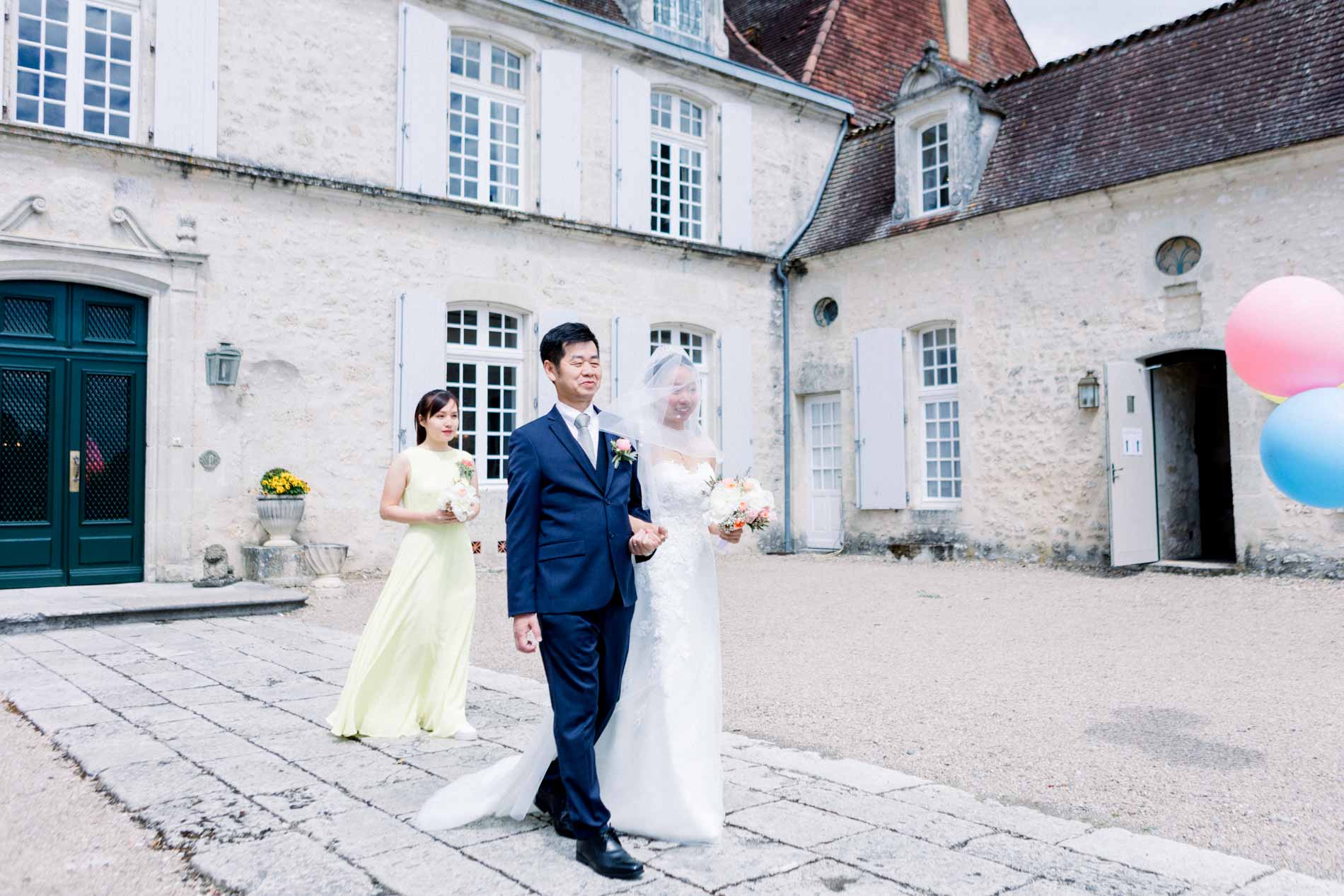 The bride walking into the courtyard of Château des Vigiers on a relative's arm