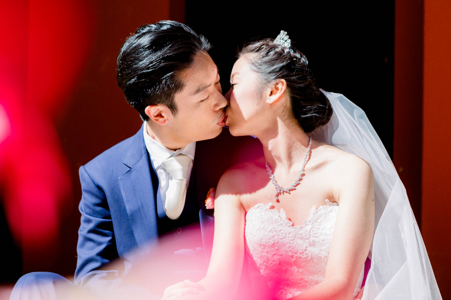 The couple kissing in front of a red curtain at Château des Vigiers