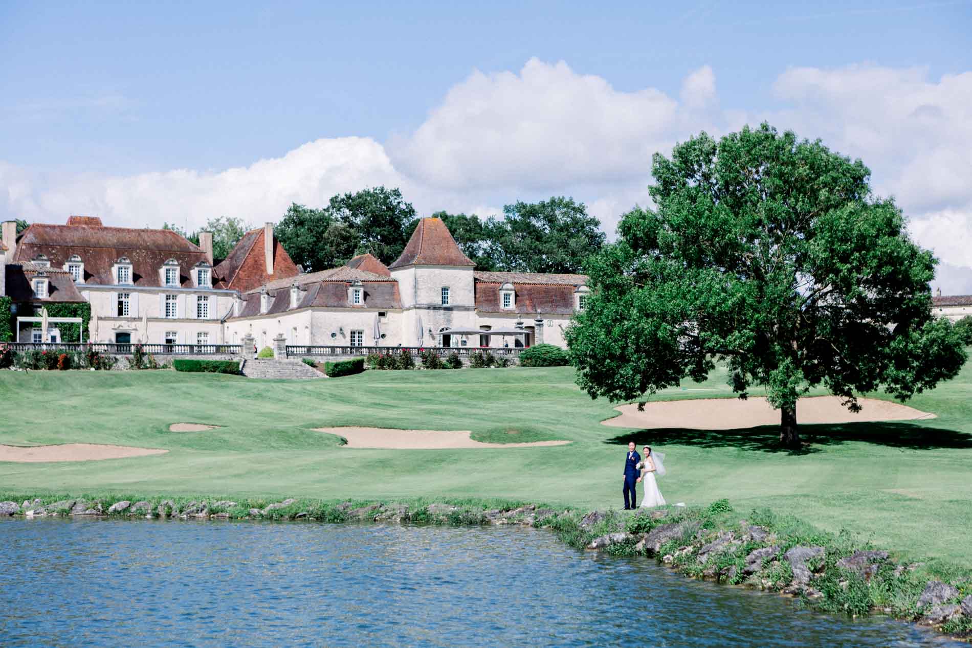 Château des Vigiers seen across the lake, with the couple at the water's edge