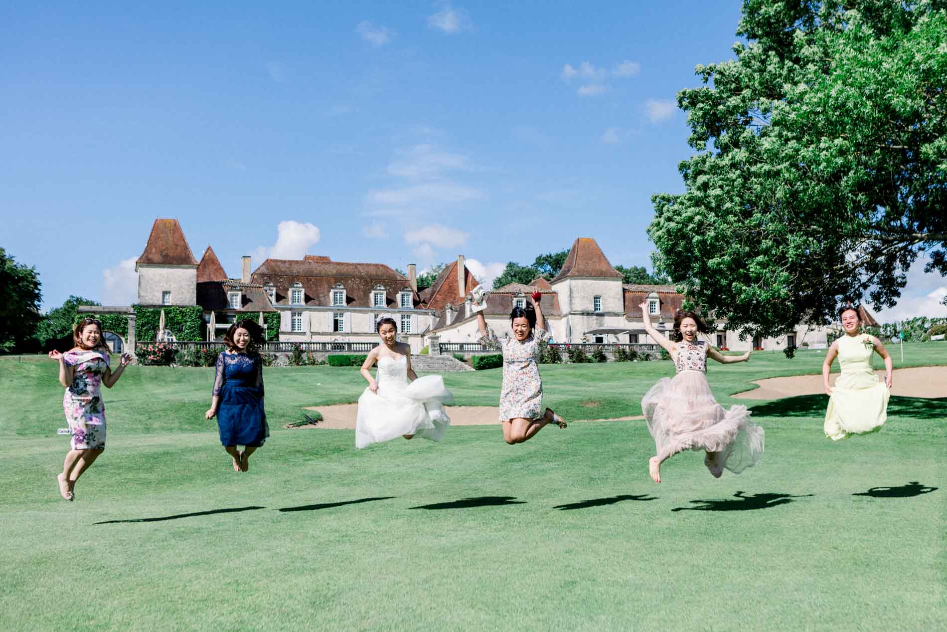 The bride and her bridesmaids jumping on the lawn facing the château