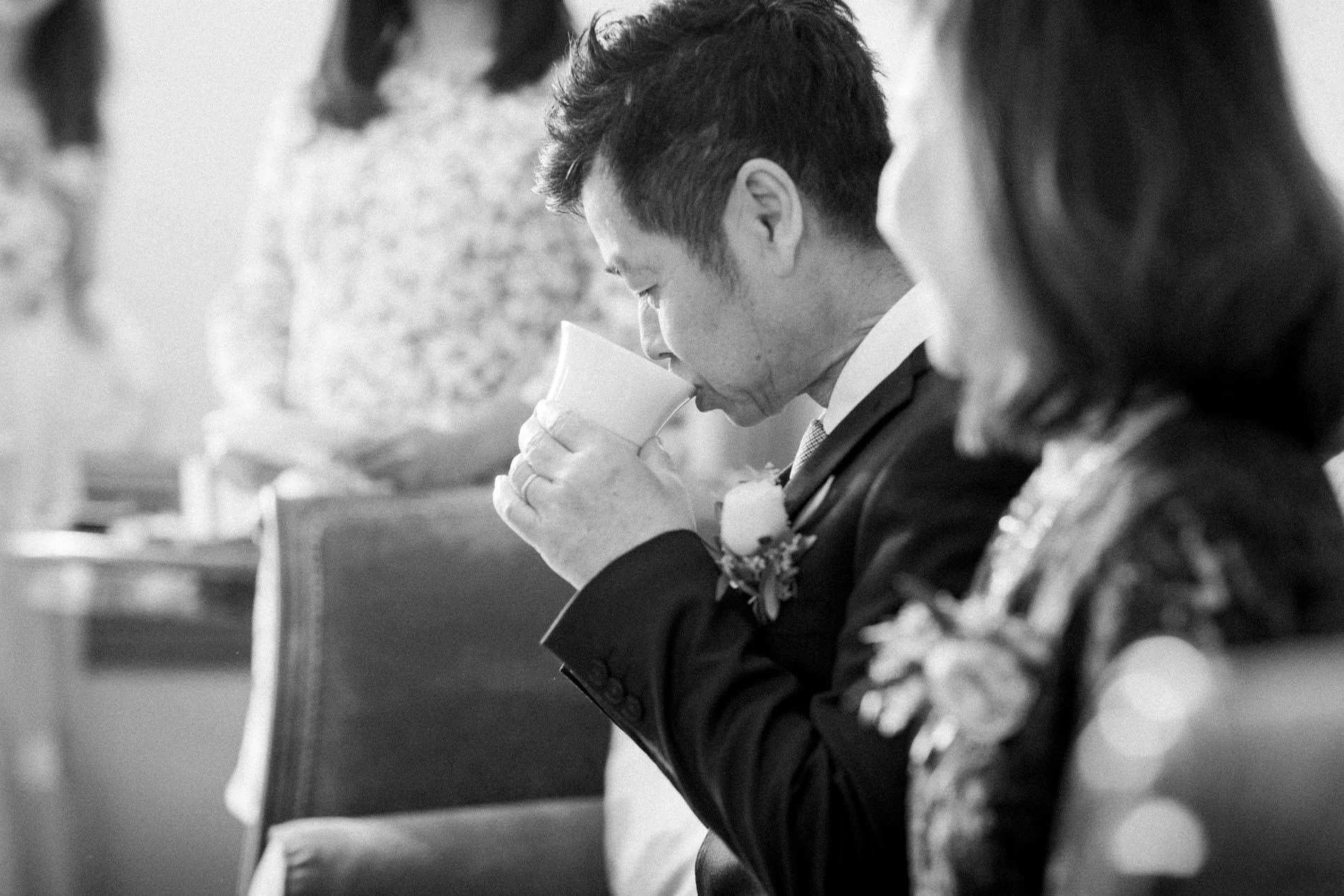 The groom sipping tea during the tea ceremony, in black and white