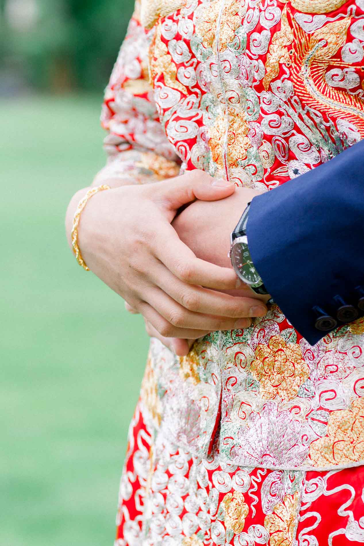 The couple's joined hands against the bride's red and gold embroidered outfit