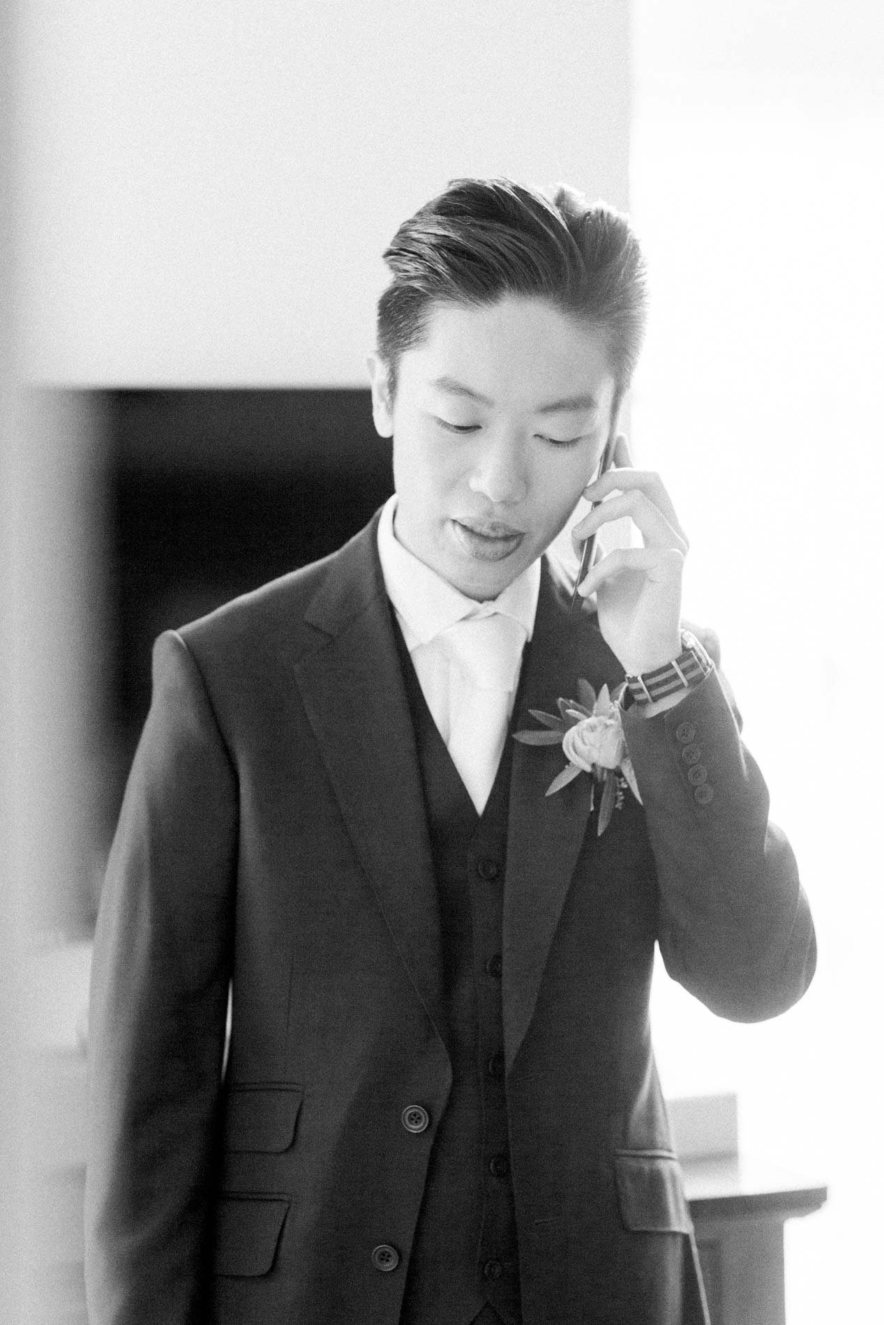 The groom on the phone in the hallway, buttonhole on his jacket, in black and white