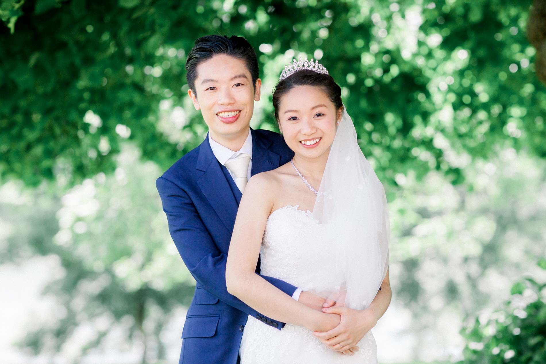 The couple embracing and smiling under the trees in the park