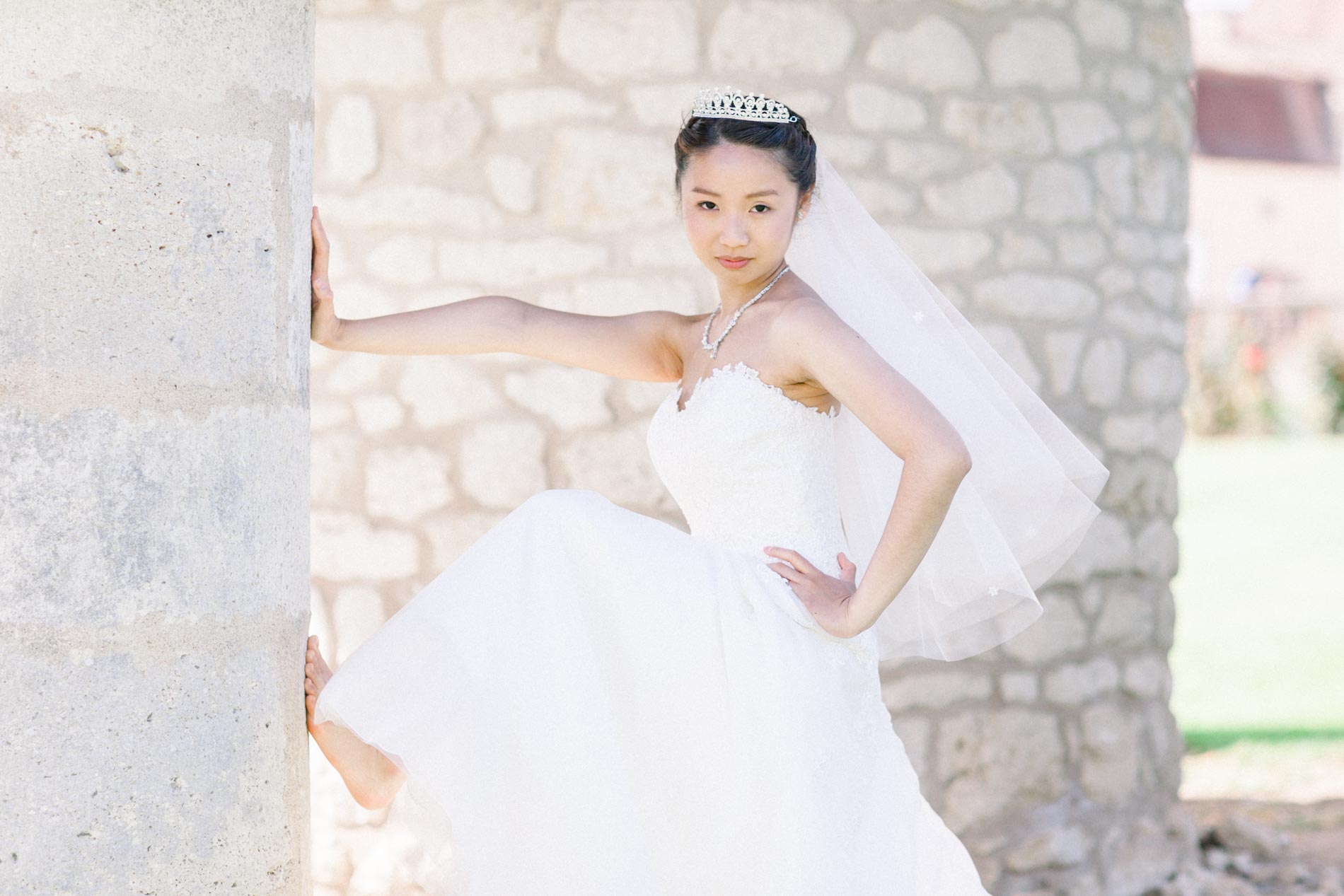 The bride striking a playful pose against a stone wall, with tiara and veil