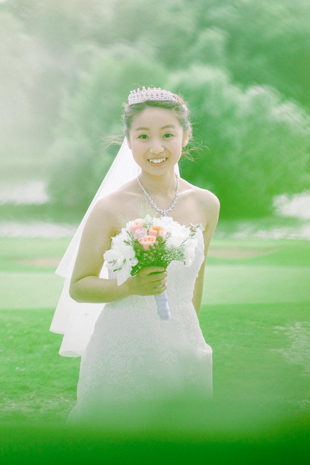The smiling bride holding her pink bouquet on the lawn