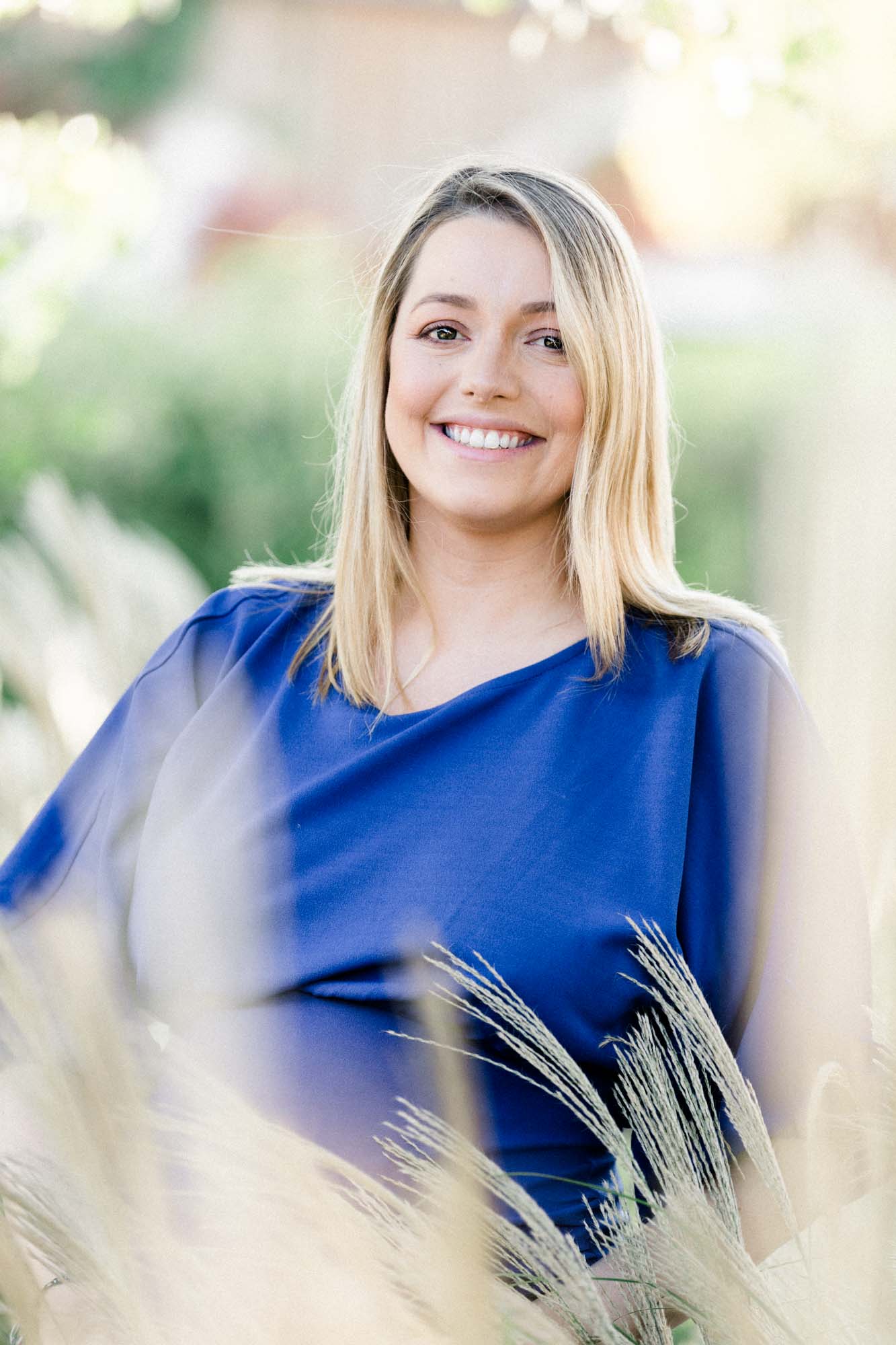Smiling mother-to-be in a blue dress among the grasses at Les Sources de Caudalie