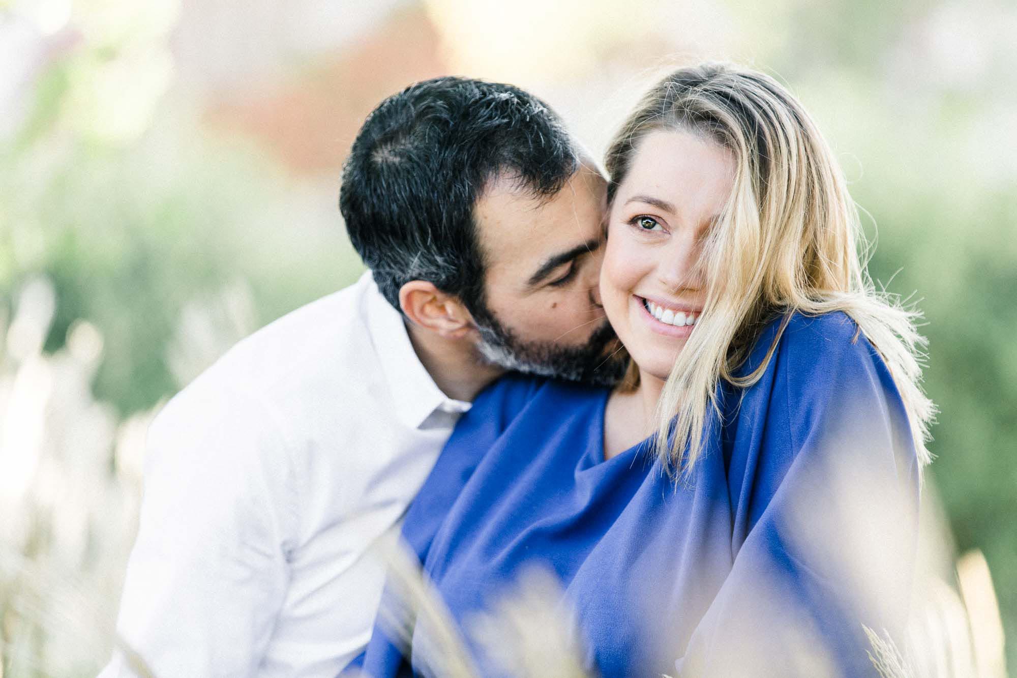 The father-to-be kissing the mother-to-be's cheek among wild grasses