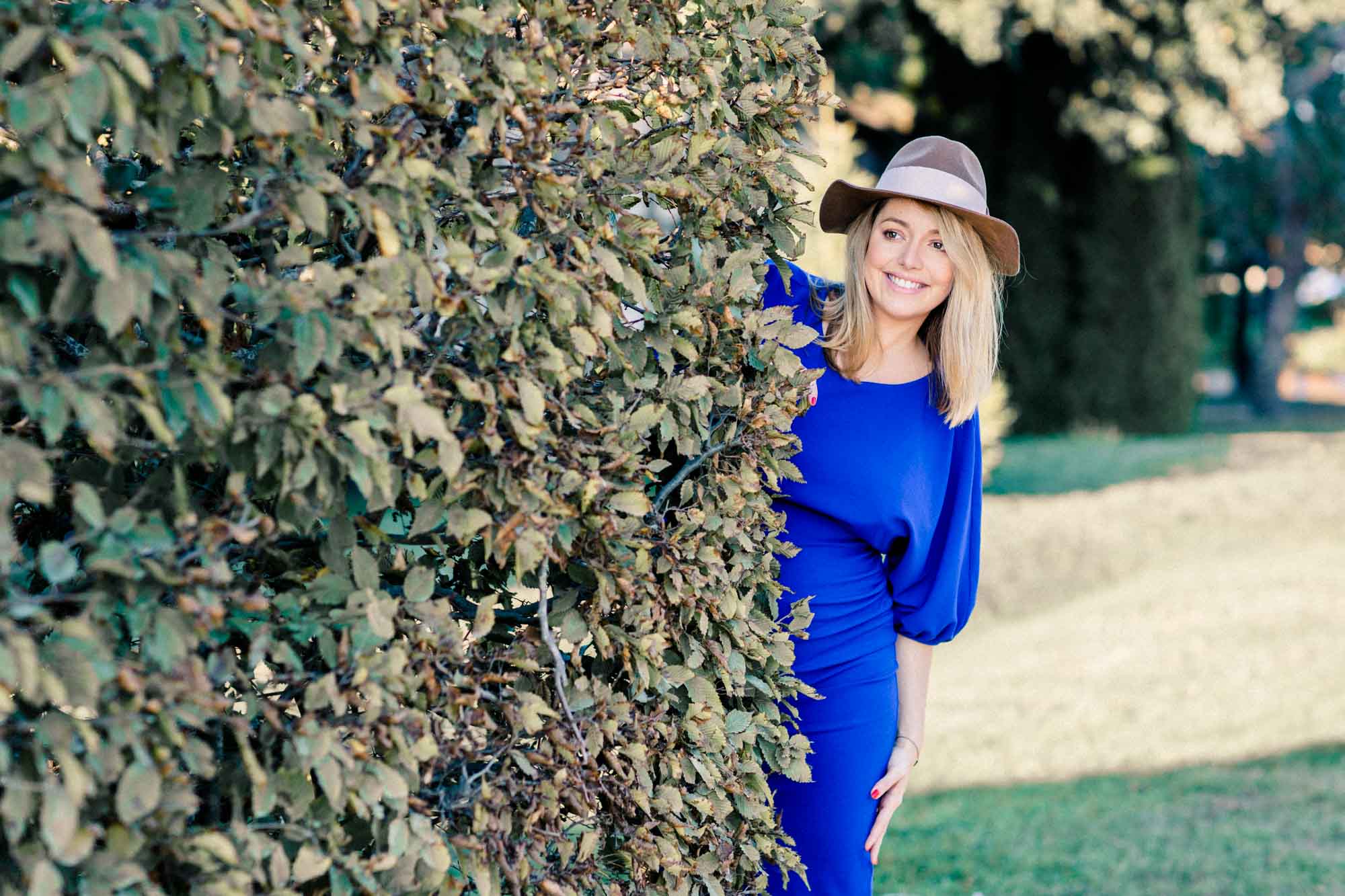 The mother-to-be in a hat peeking out from behind a leafy hedge