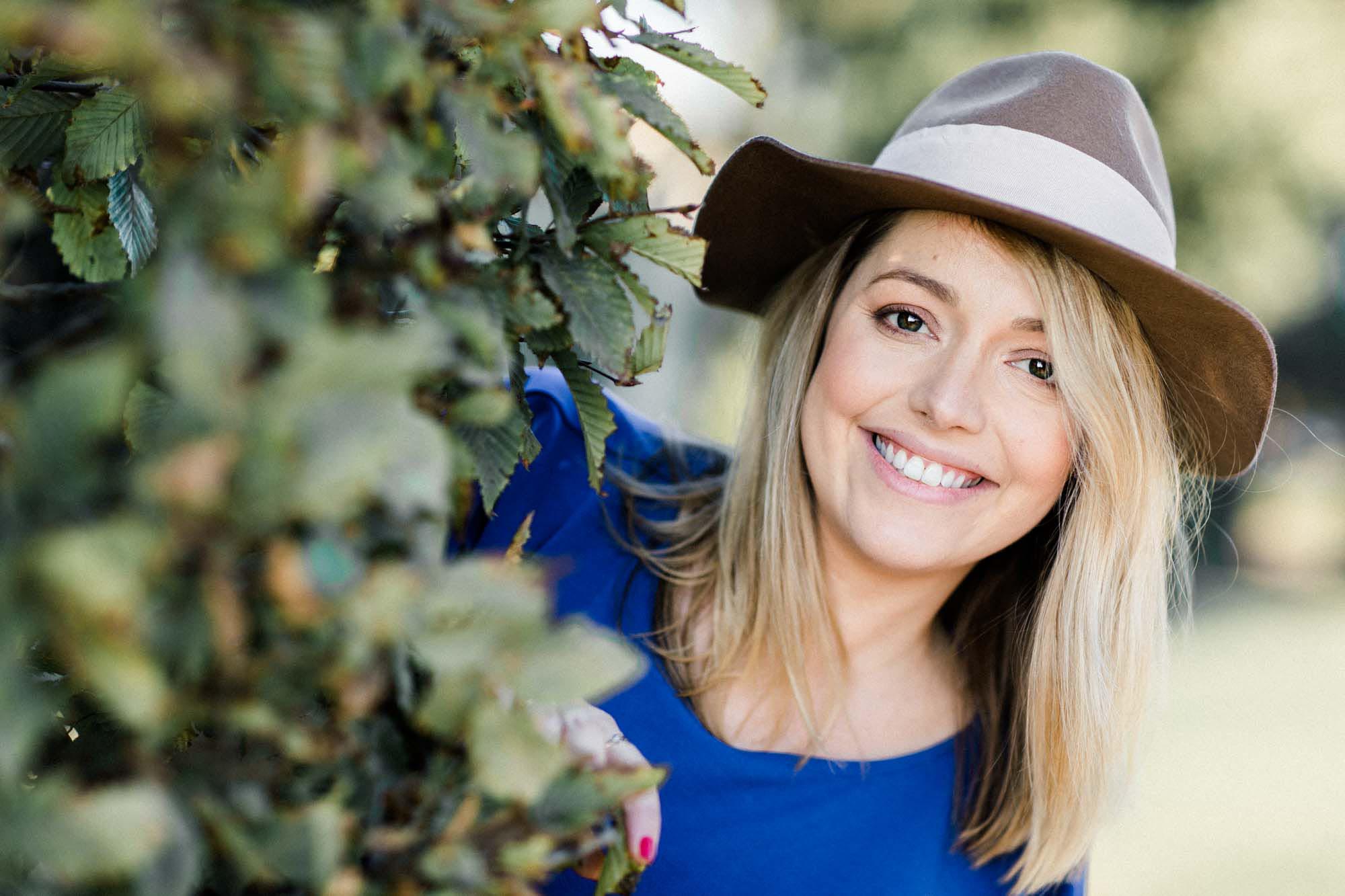The mother-to-be in a hat smiling between the leaves
