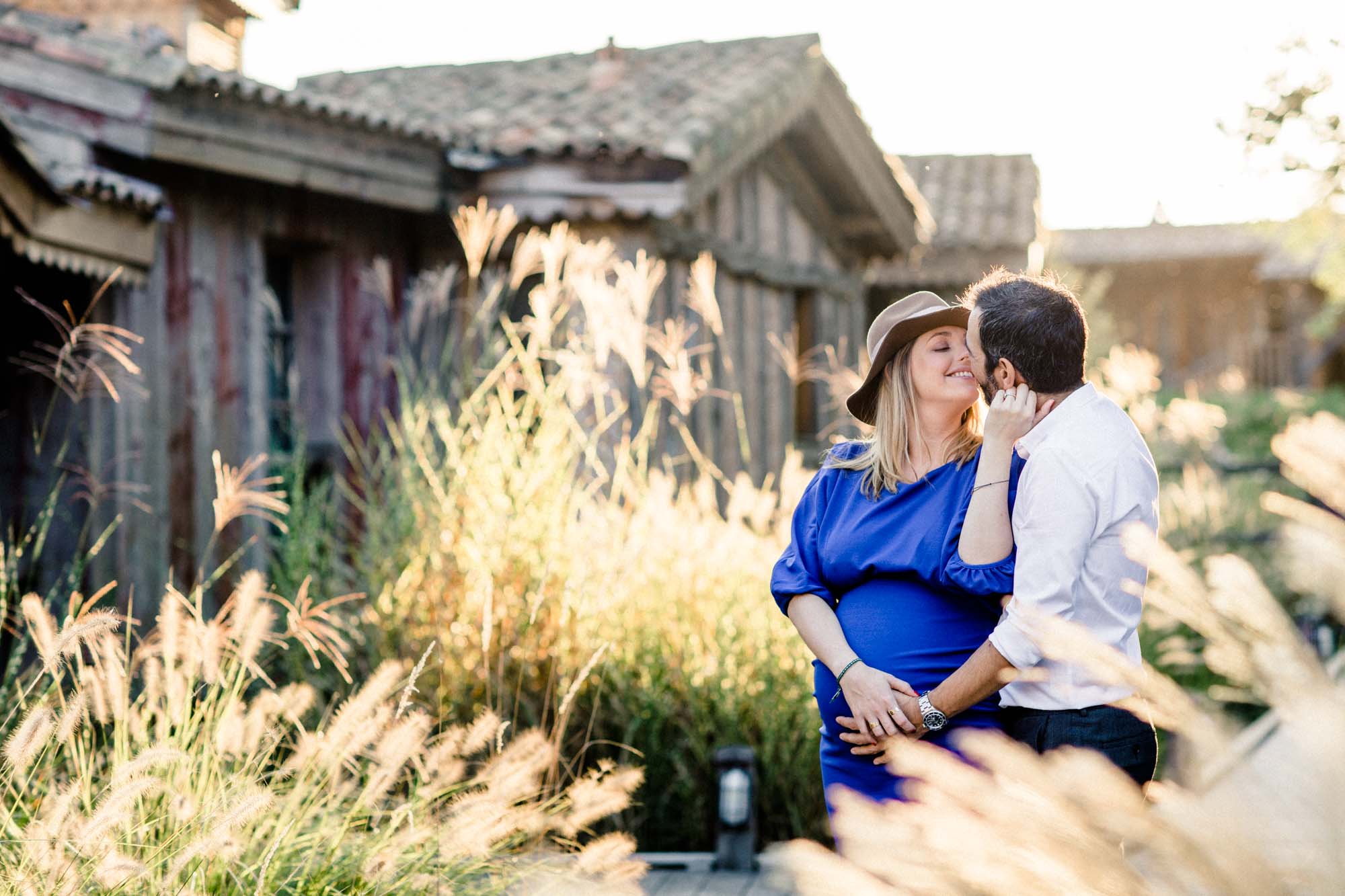 The couple embracing among grasses before the wooden buildings of Les Sources de Caudalie