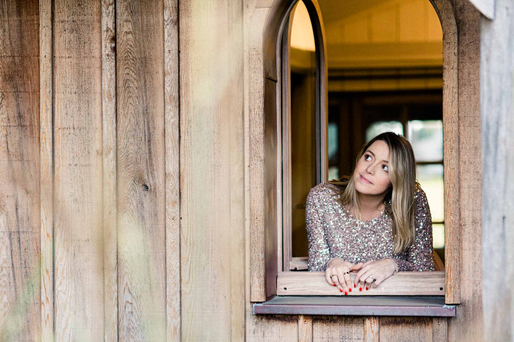 The mother-to-be in a sequinned dress leaning on a wooden window sill