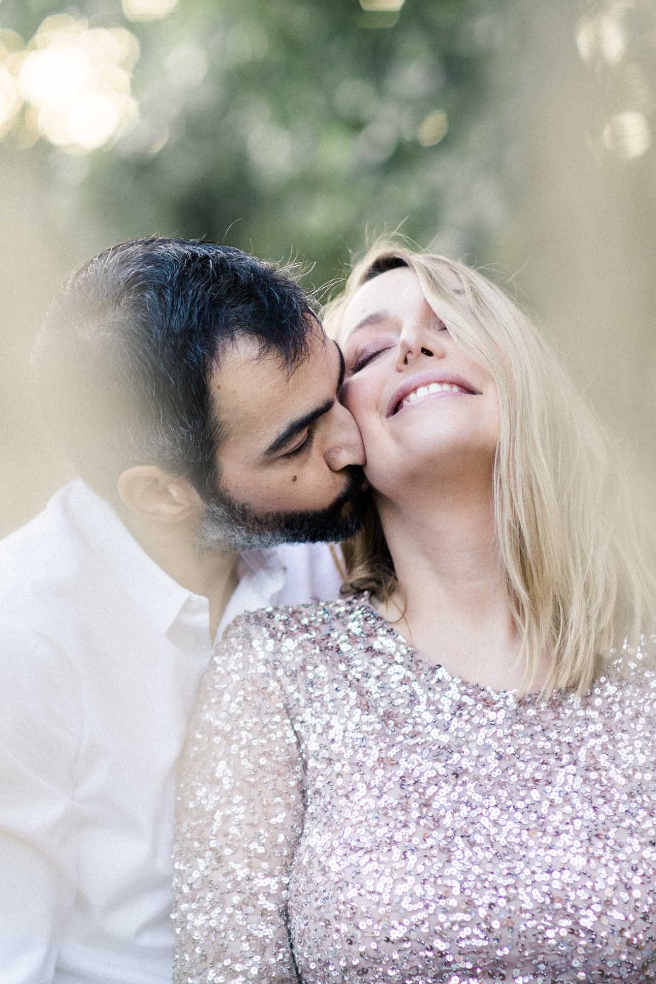 The father-to-be kissing the cheek of the mother-to-be in her sequinned dress
