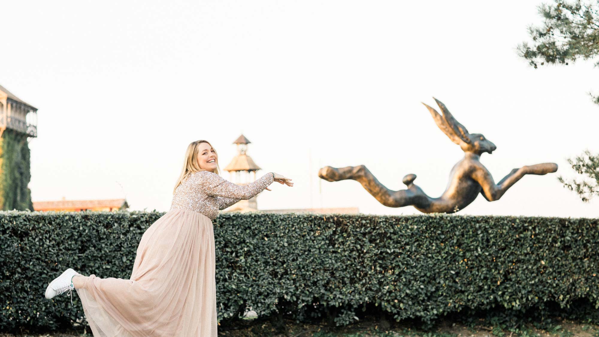 The mother-to-be playfully mimicking the leaping hare sculpture above the hedge