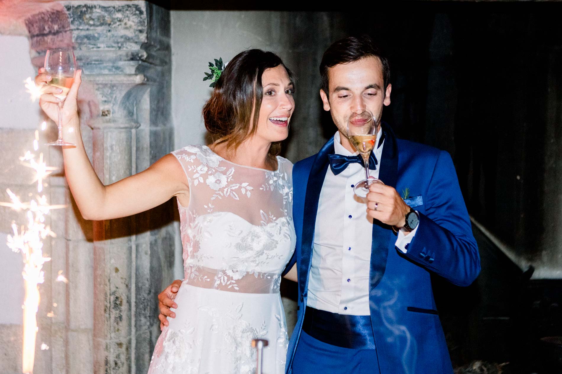 Bride and groom raising their glasses beside sparklers at the evening party
