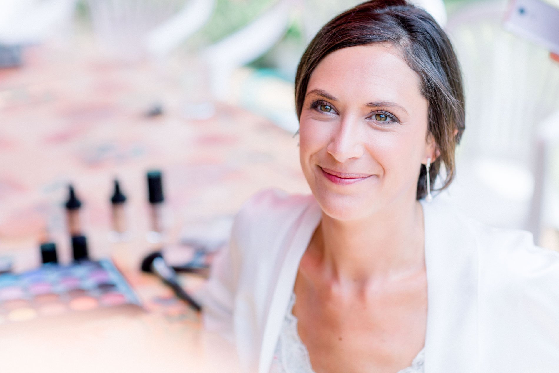 Bride smiling during final preparations, make-up products blurred in the foreground