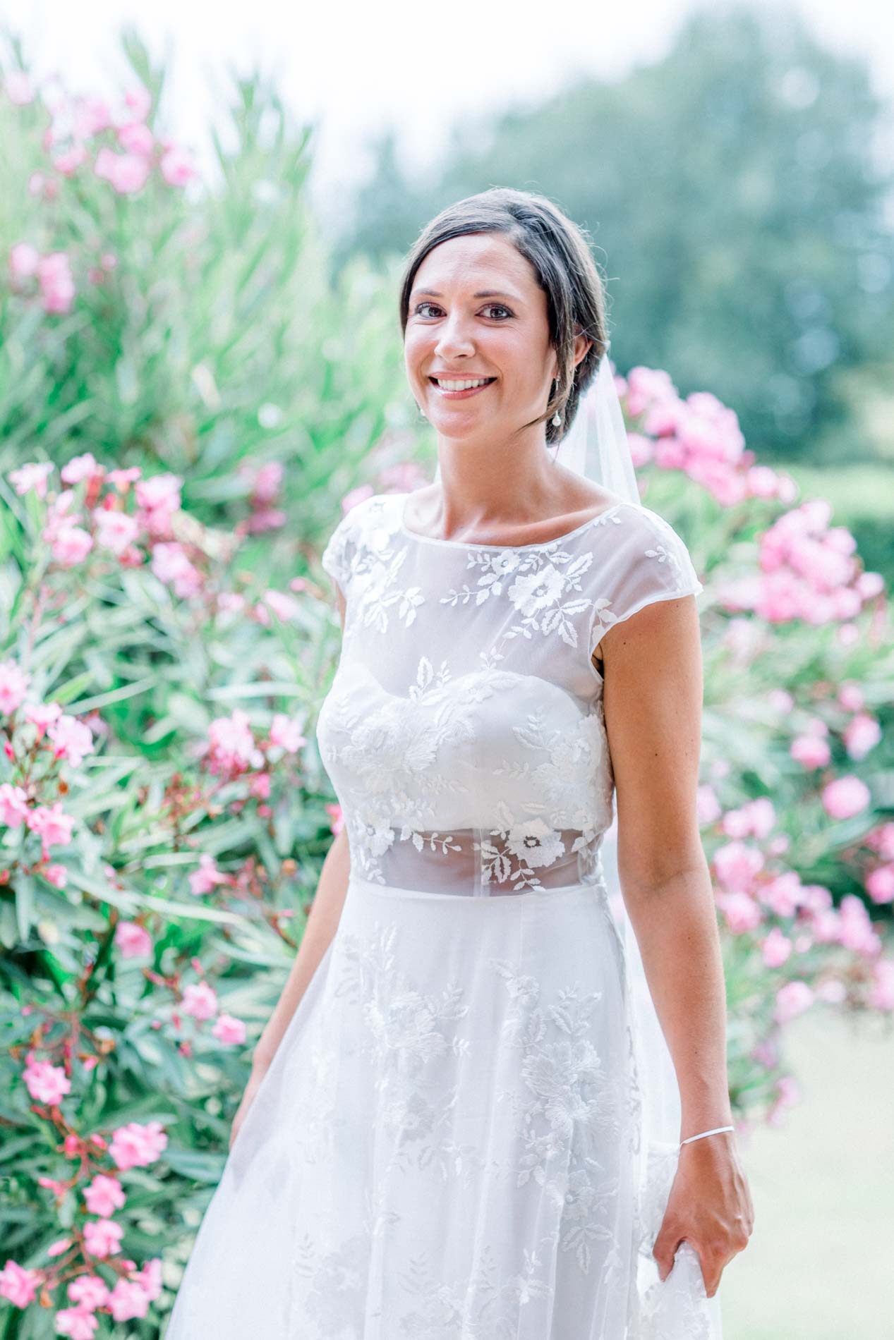 Bride posing before flowering oleanders in her embroidered gown and veil