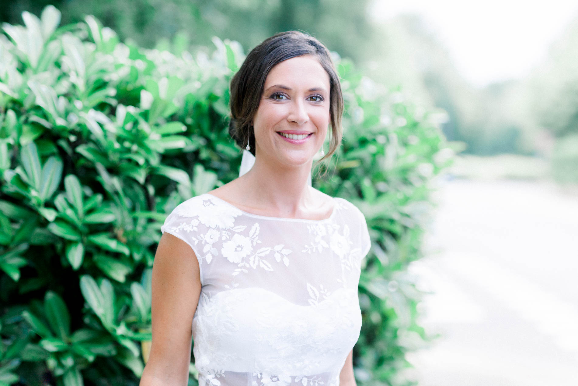 Bride with a radiant smile in front of a lush green hedge