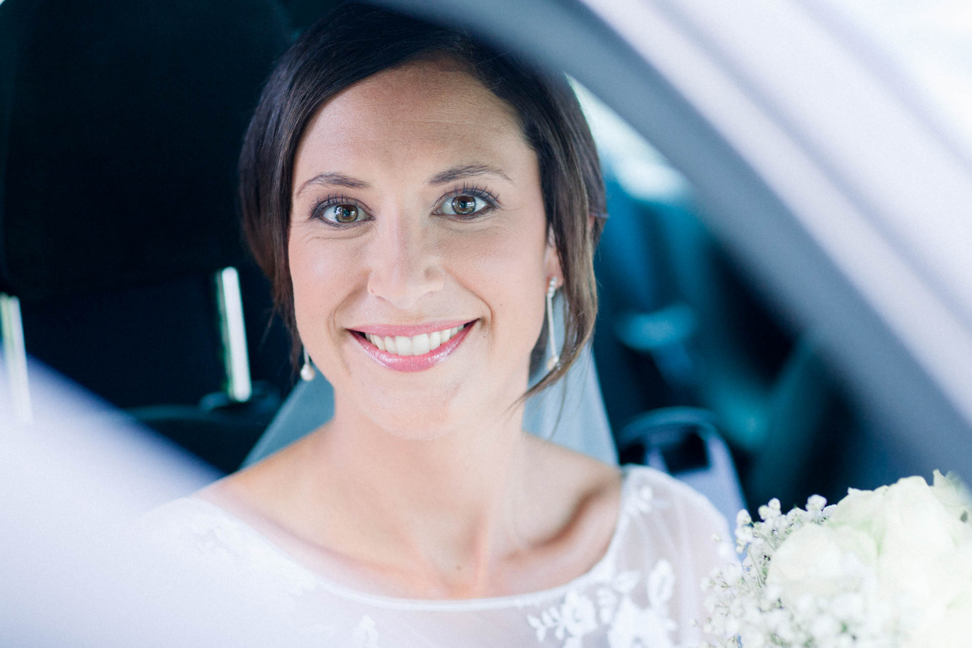 Smiling bride in the car with a baby's breath bouquet on her lap