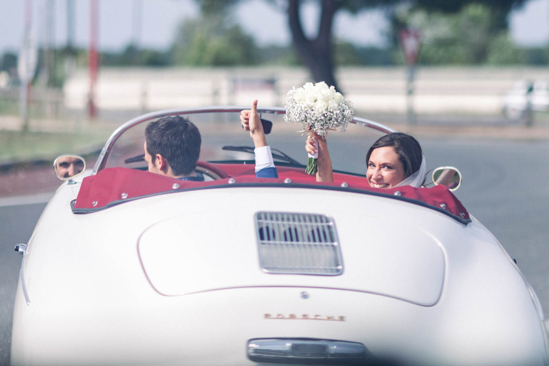 Bride and groom raising their arms in a white vintage convertible after the ceremony