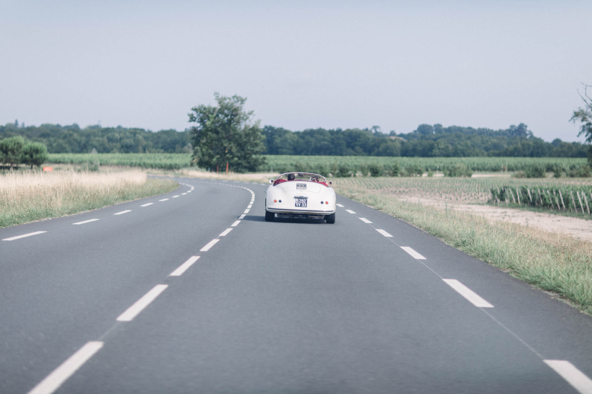 The couple's white convertible driving along a road lined with vineyards