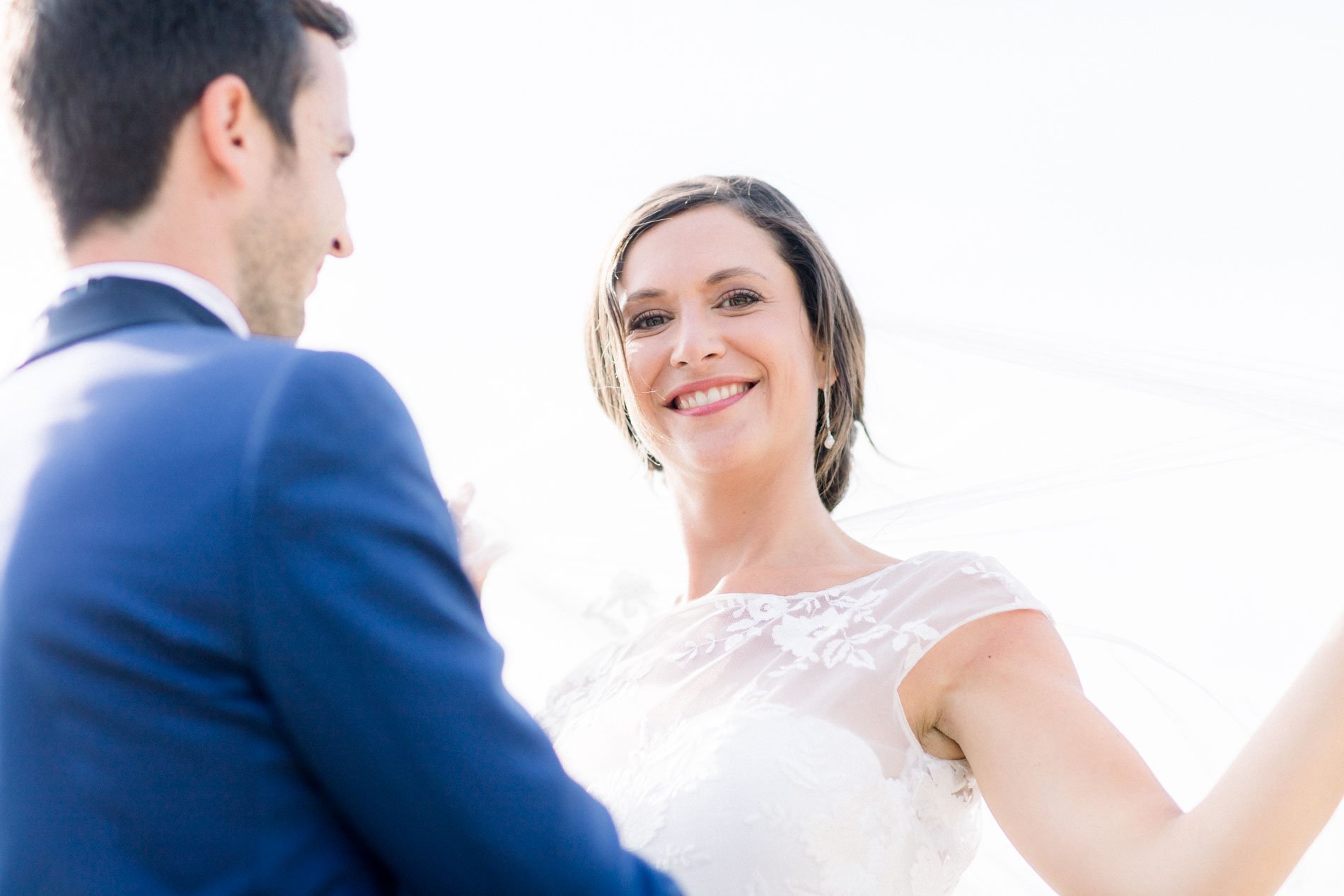 Bride twirling her veil toward the groom in soft summer light
