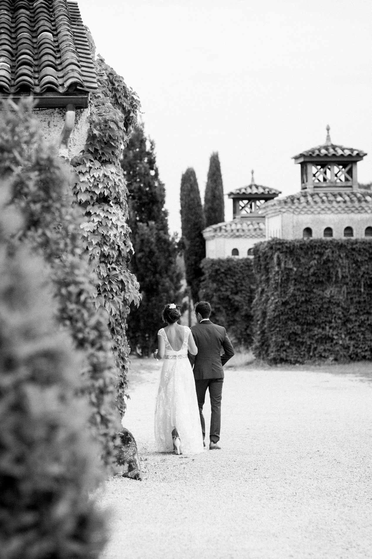 Bride and groom walking down an ivy-lined path, black and white