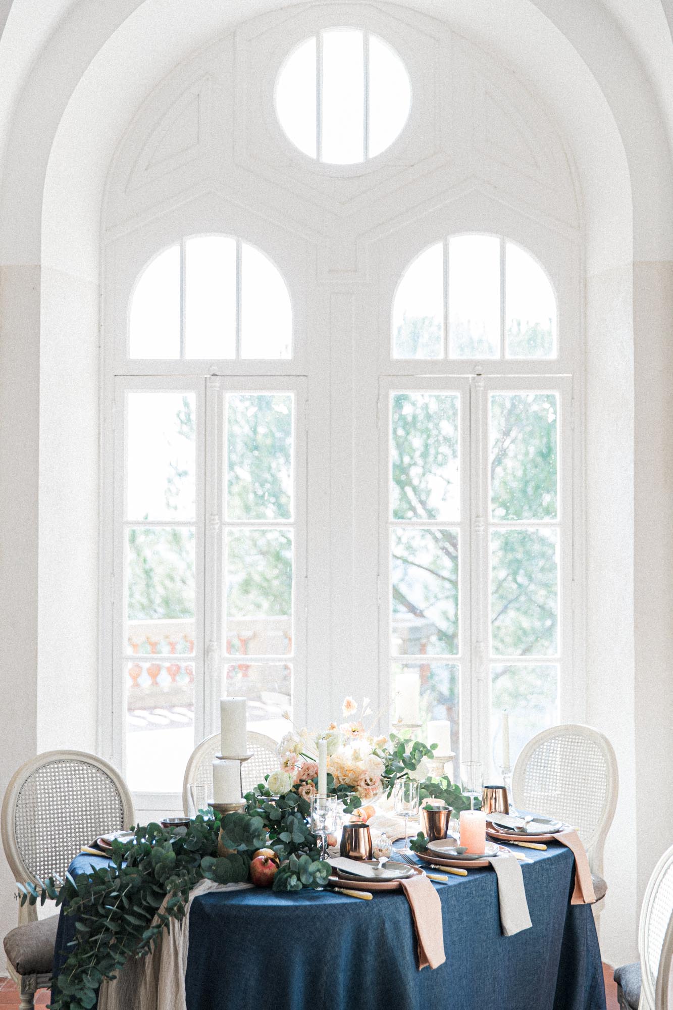 Table de mariage dressée en bleu nuit sous de grandes fenêtres cintrées