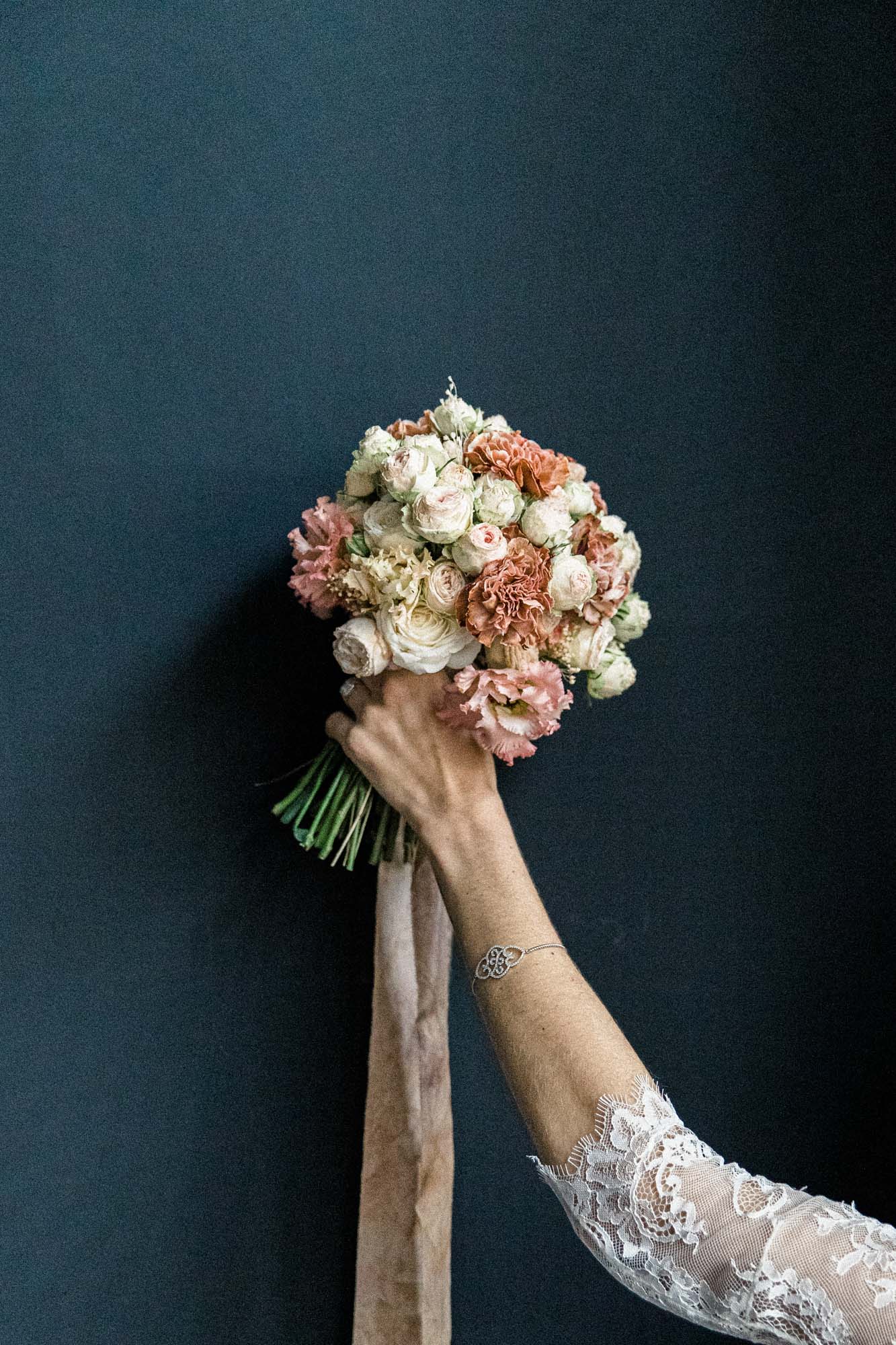 Main de la mariée tenant un bouquet de roses devant un mur bleu nuit