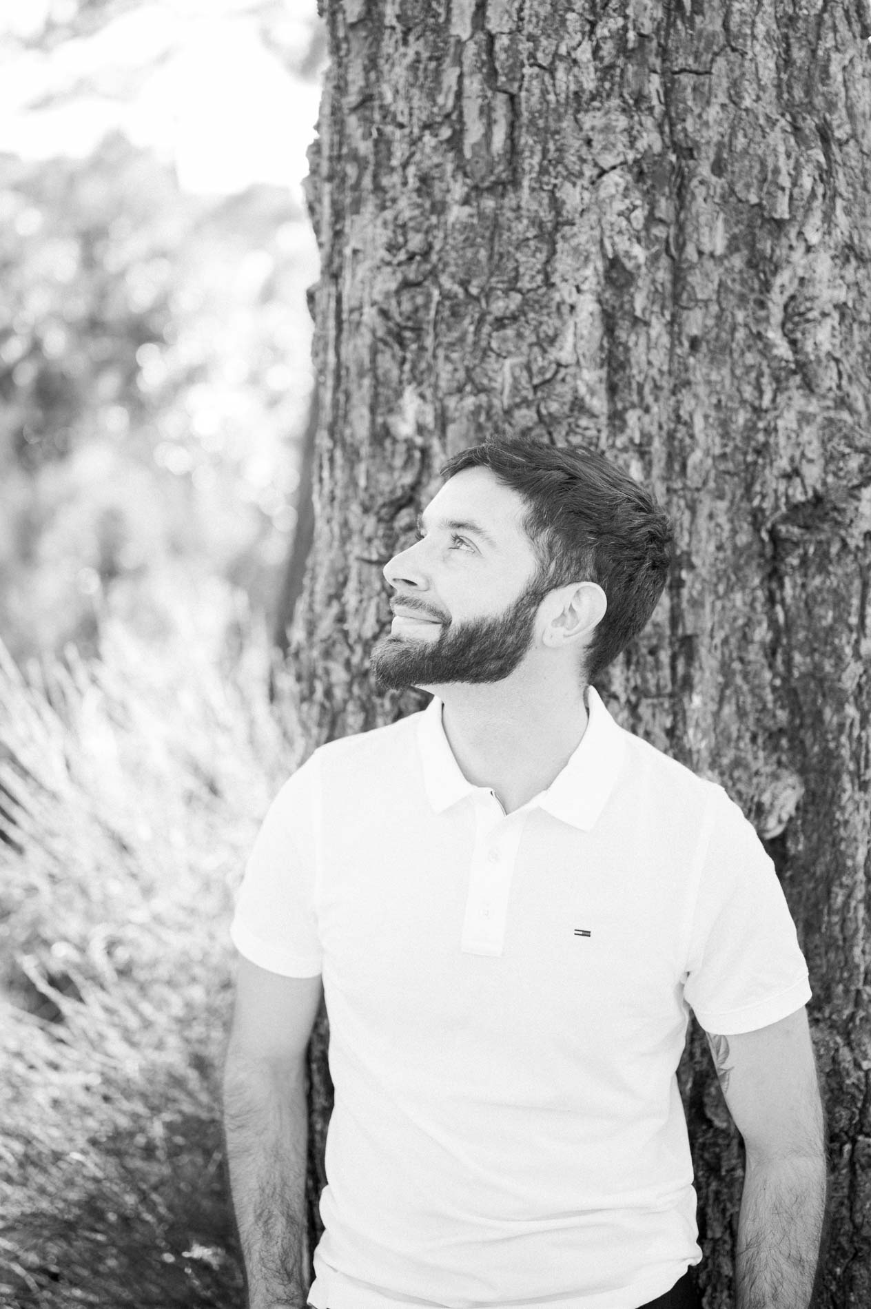 Black and white portrait of a bearded man against a pine trunk