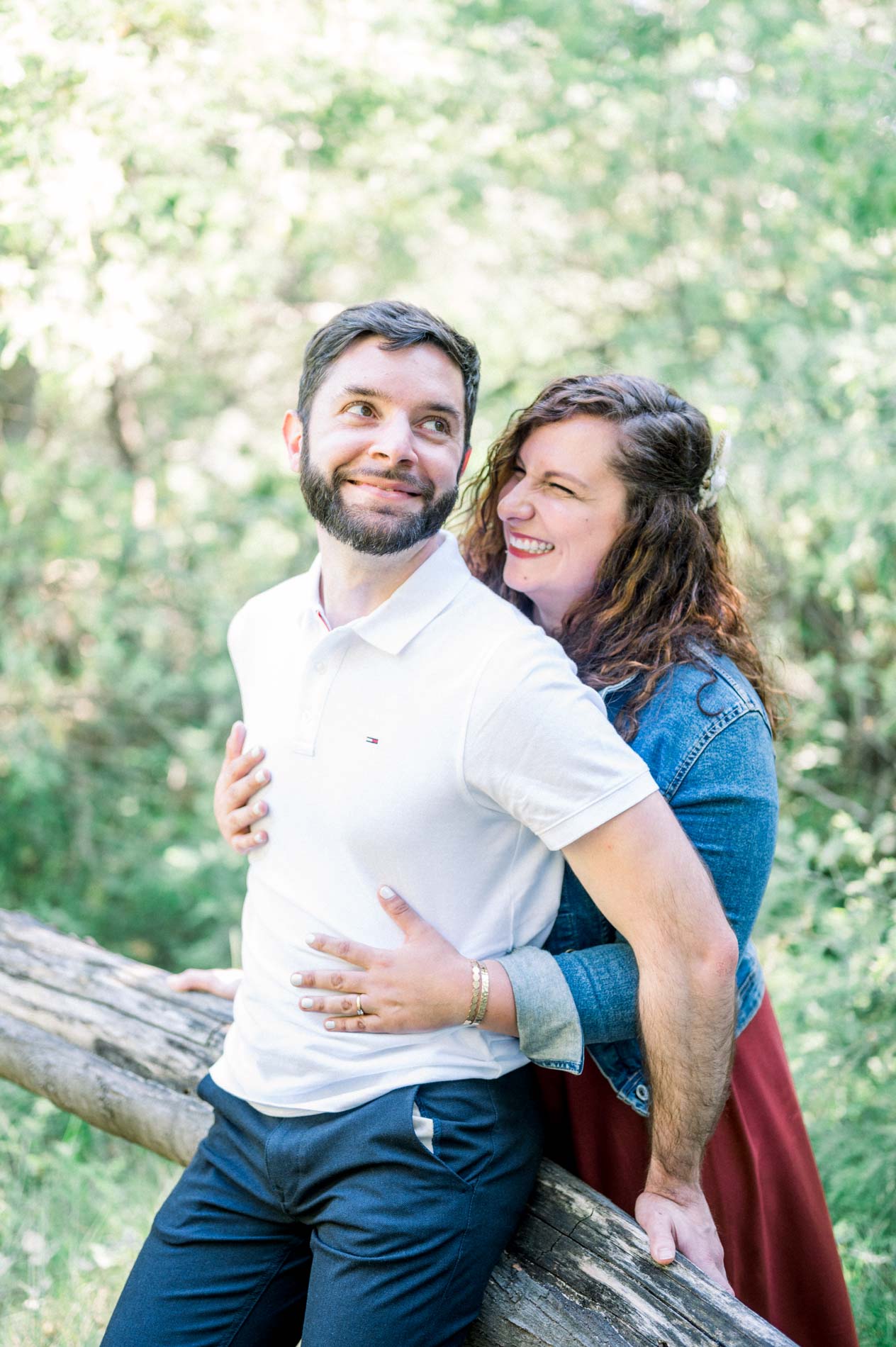 Woman hugging her partner seated on a log in the forest