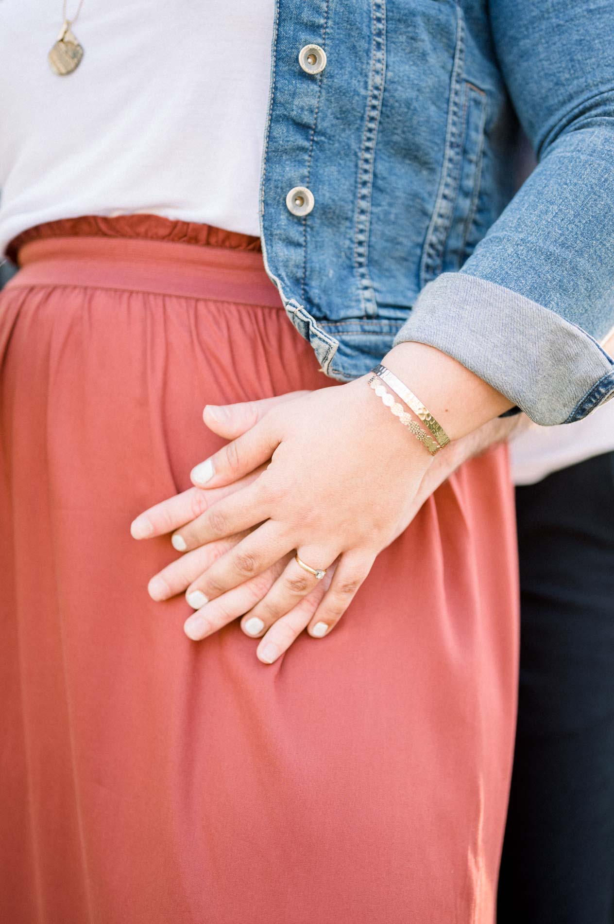 Couple's hands intertwined on the red skirt, engagement ring visible