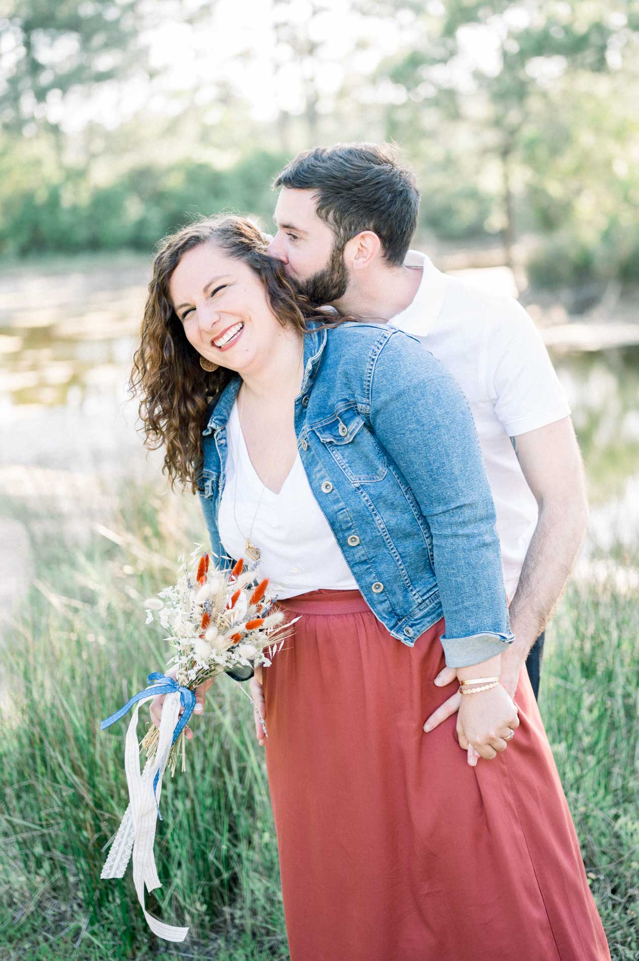 Couple embracing in the grass beside a pond, bouquet in hand