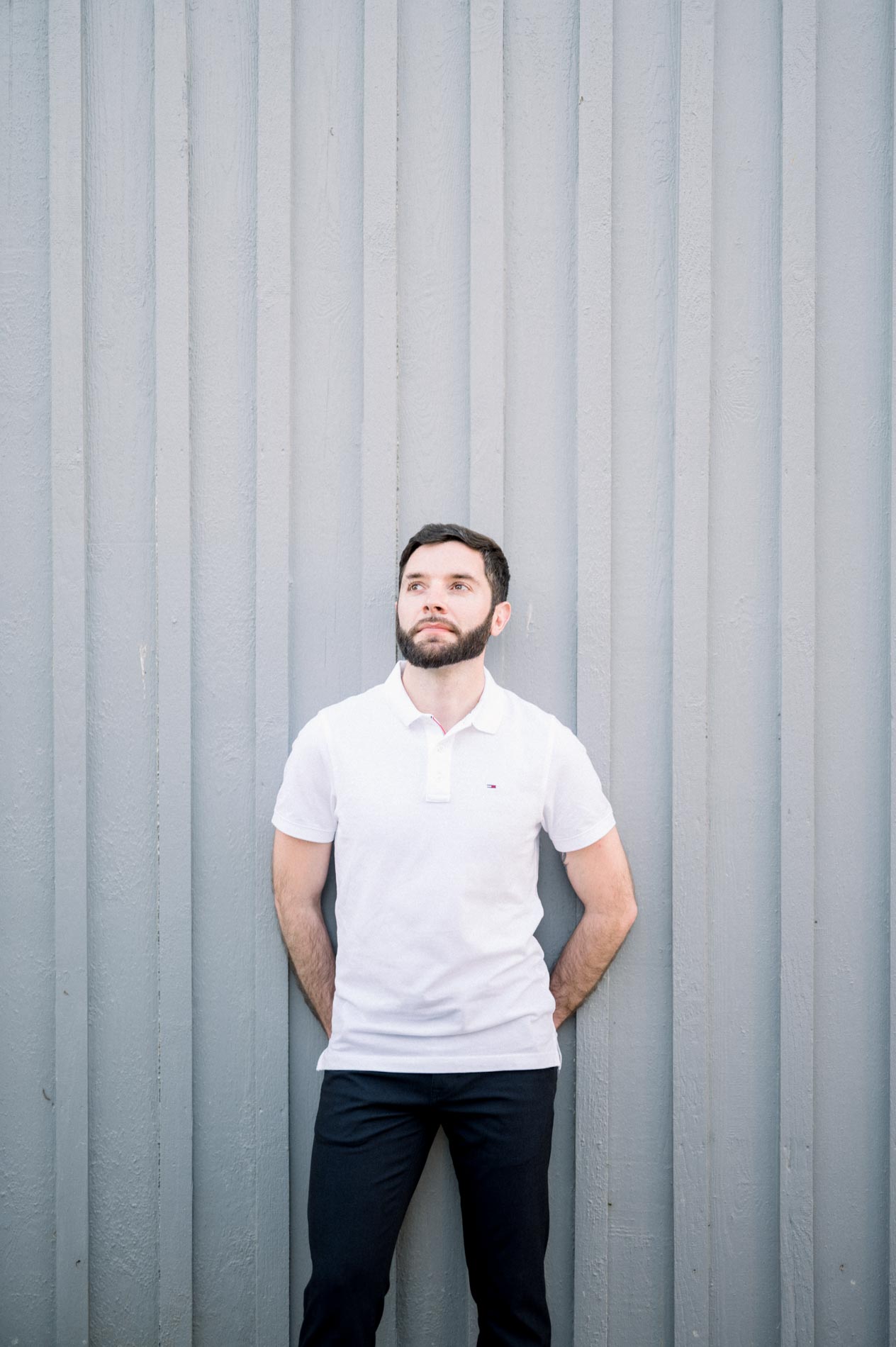 Portrait of a man in a white polo against a grey wooden wall