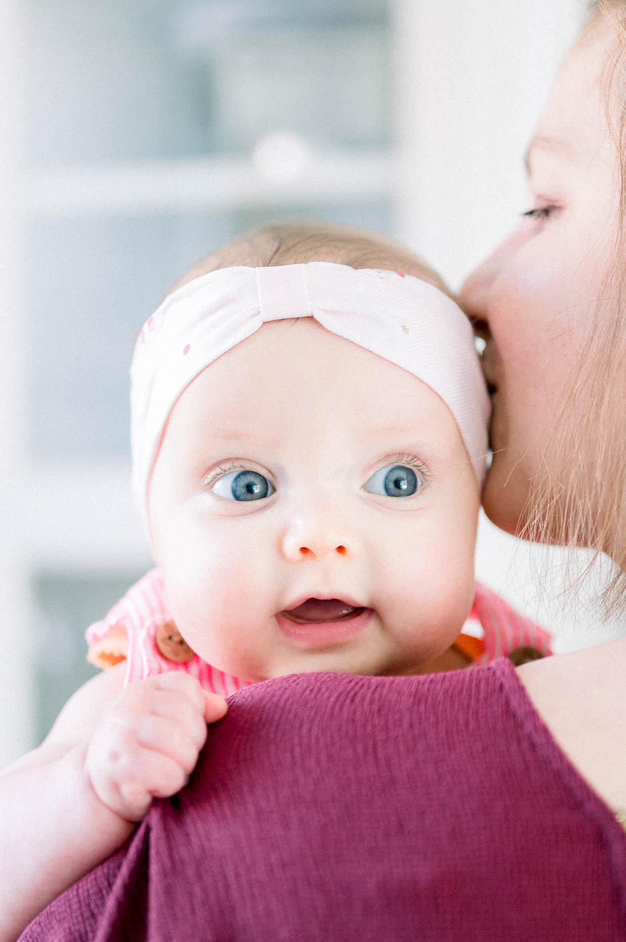 Baby in a pink headband being kissed on the head by her mum