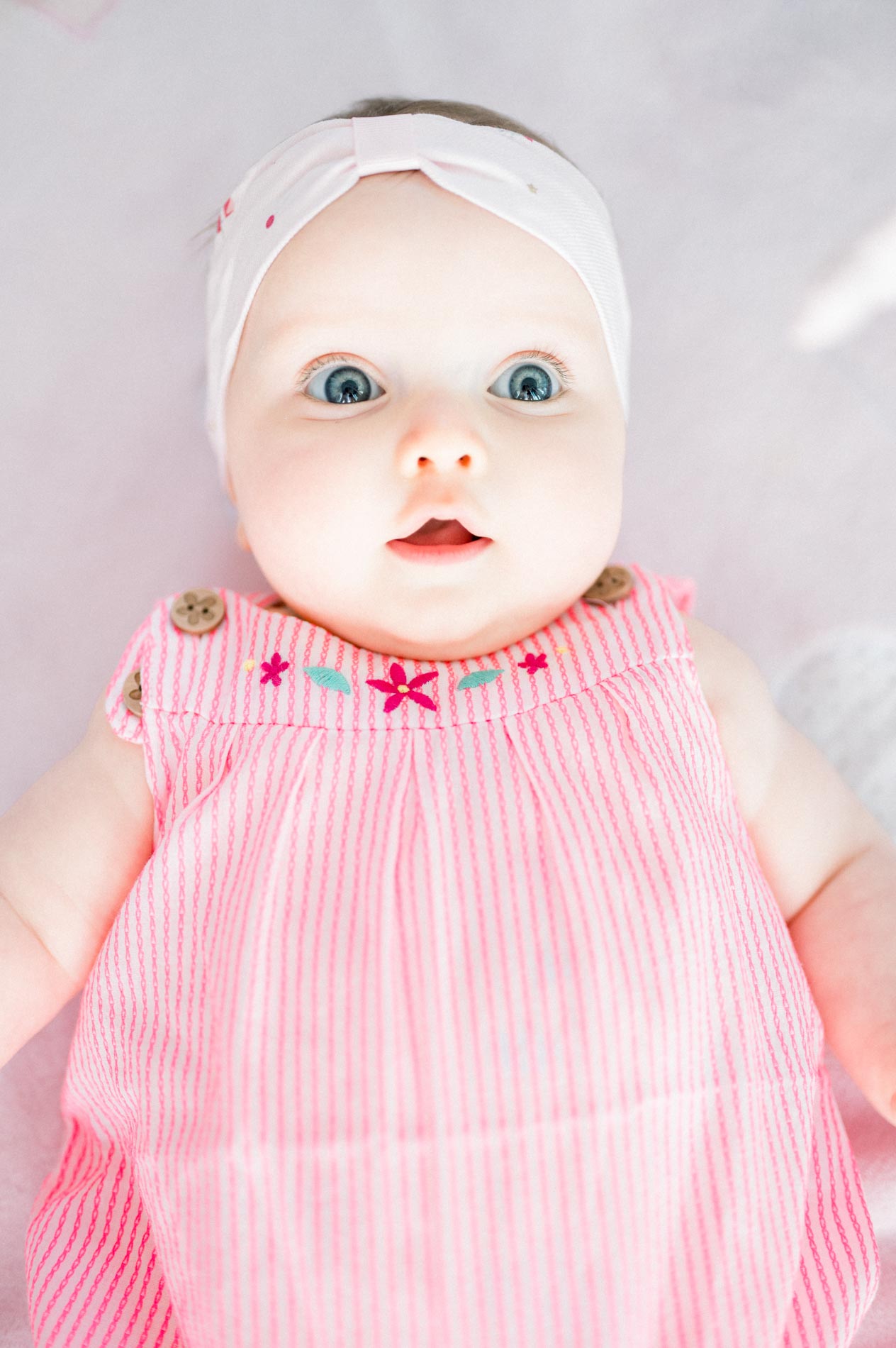 Baby in a pink romper and headband lying down, looking at the camera