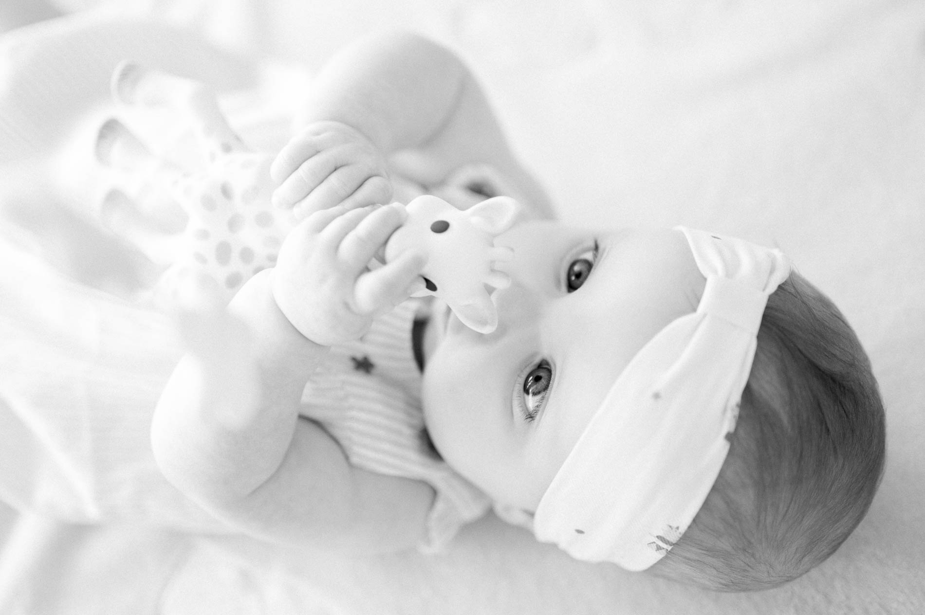 Baby in a headband chewing a teething giraffe, in black and white