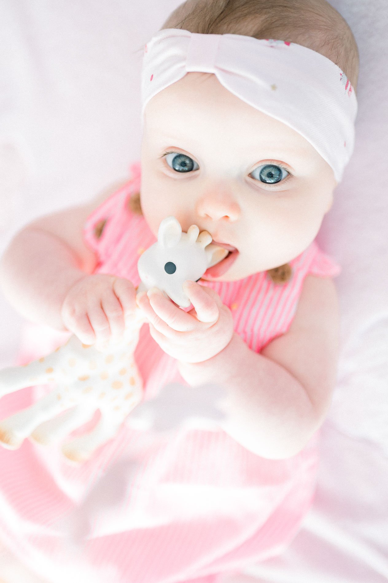Baby in pink chewing her teething giraffe, seen from above