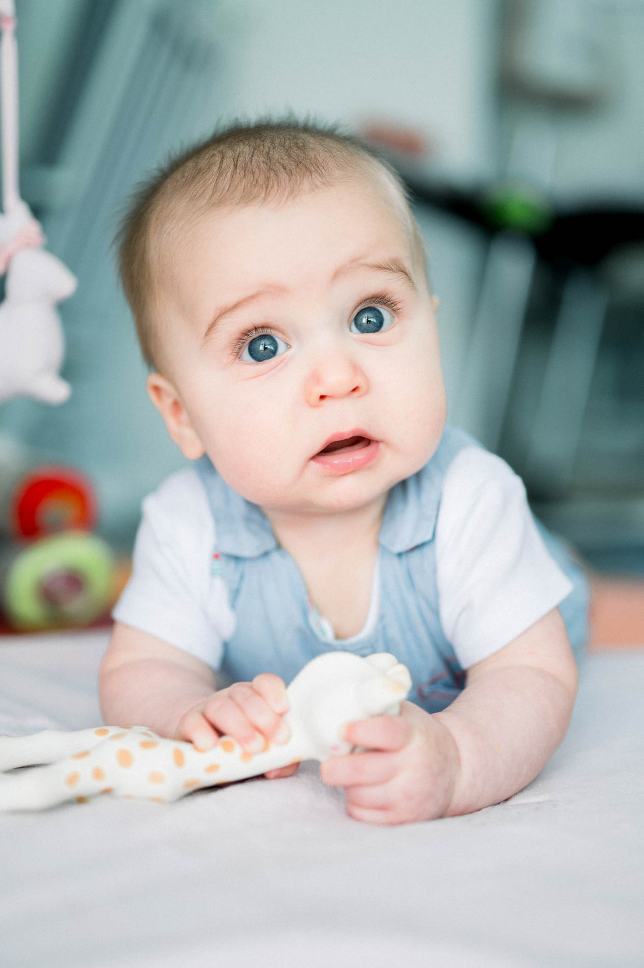 Baby in a blue shirt on his tummy, looking wide-eyed at the camera