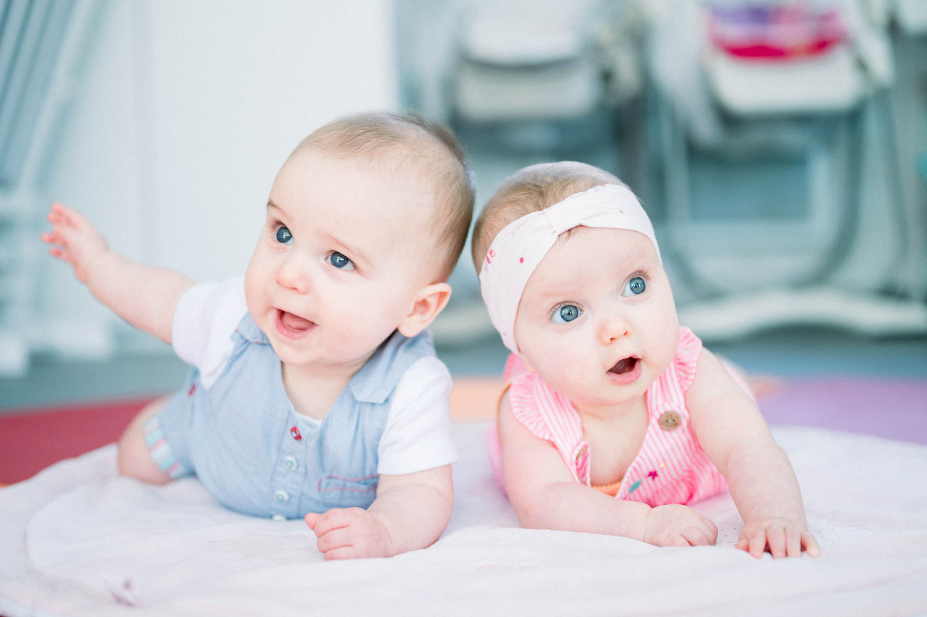 Two babies in blue and pink lifting their heads on their mat