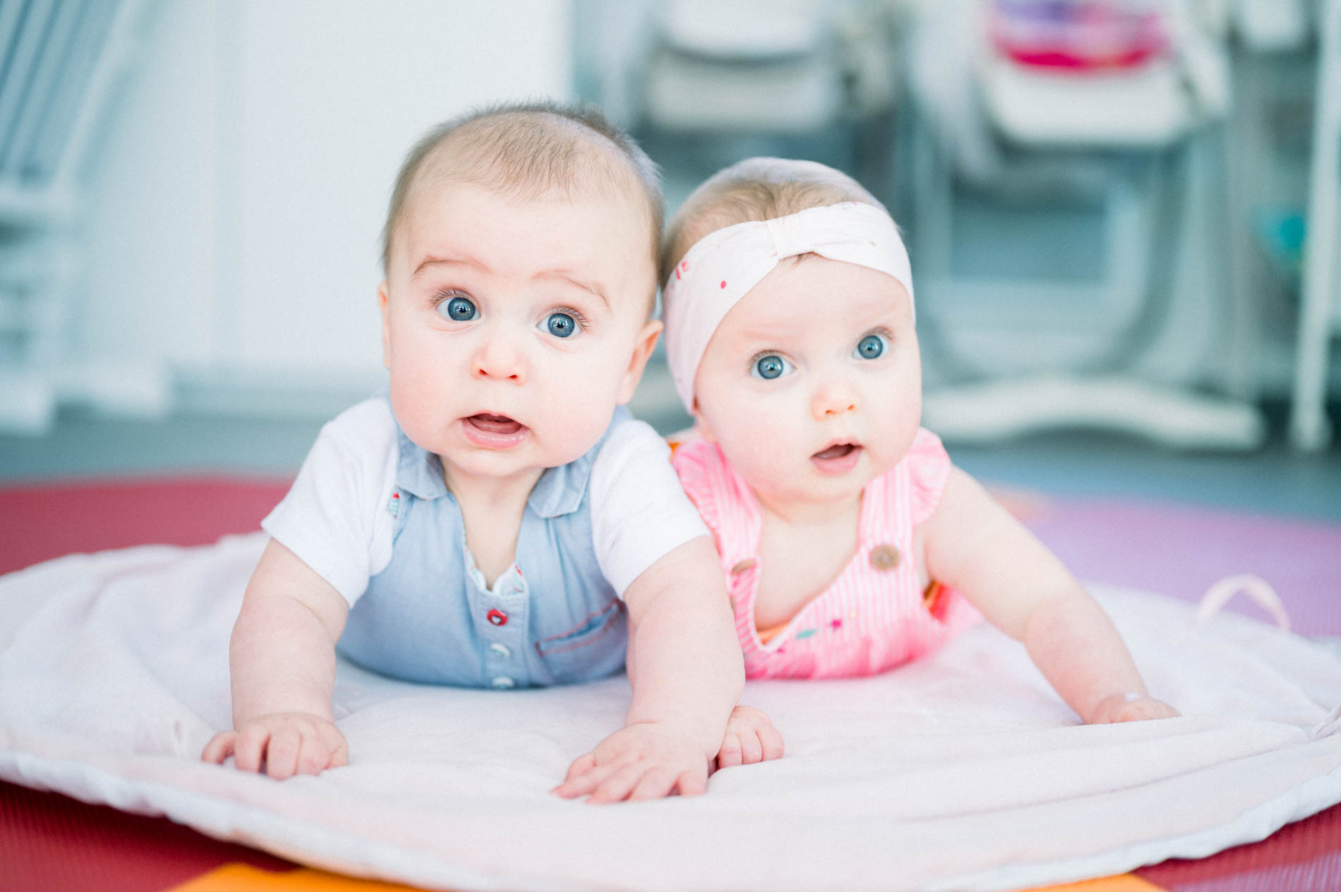 Two babies lying on their tummies side by side on a play mat during an at-home baby session