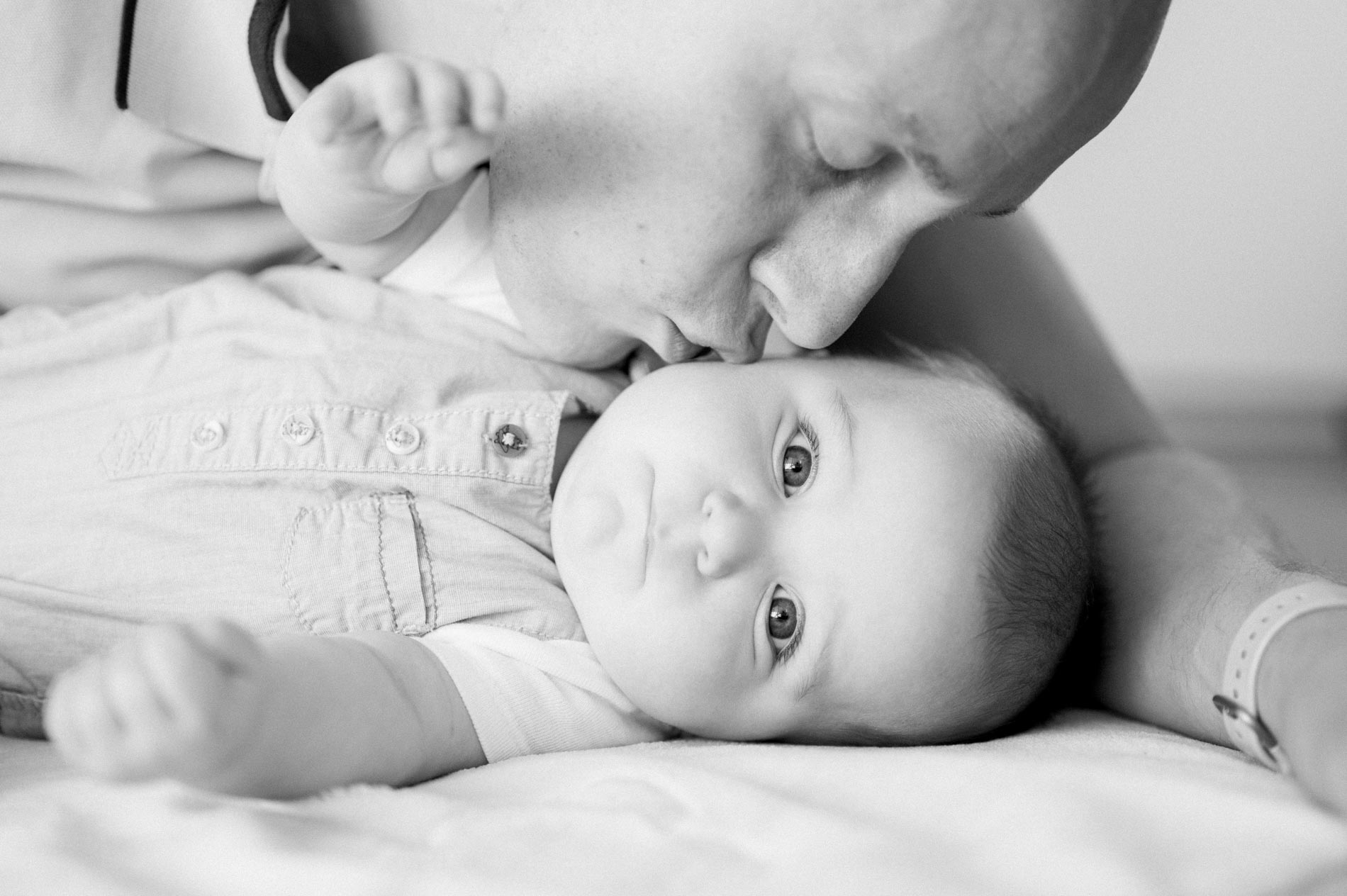 Dad kissing his baby lying on the bed, in black and white